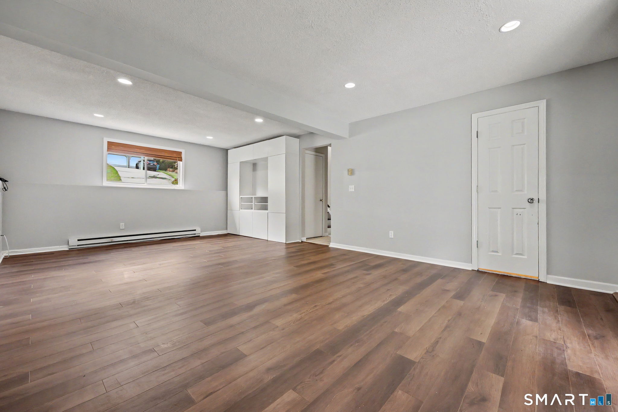 Empty finished room with brown wood-look flooring, gray walls, and built-in white shelving.