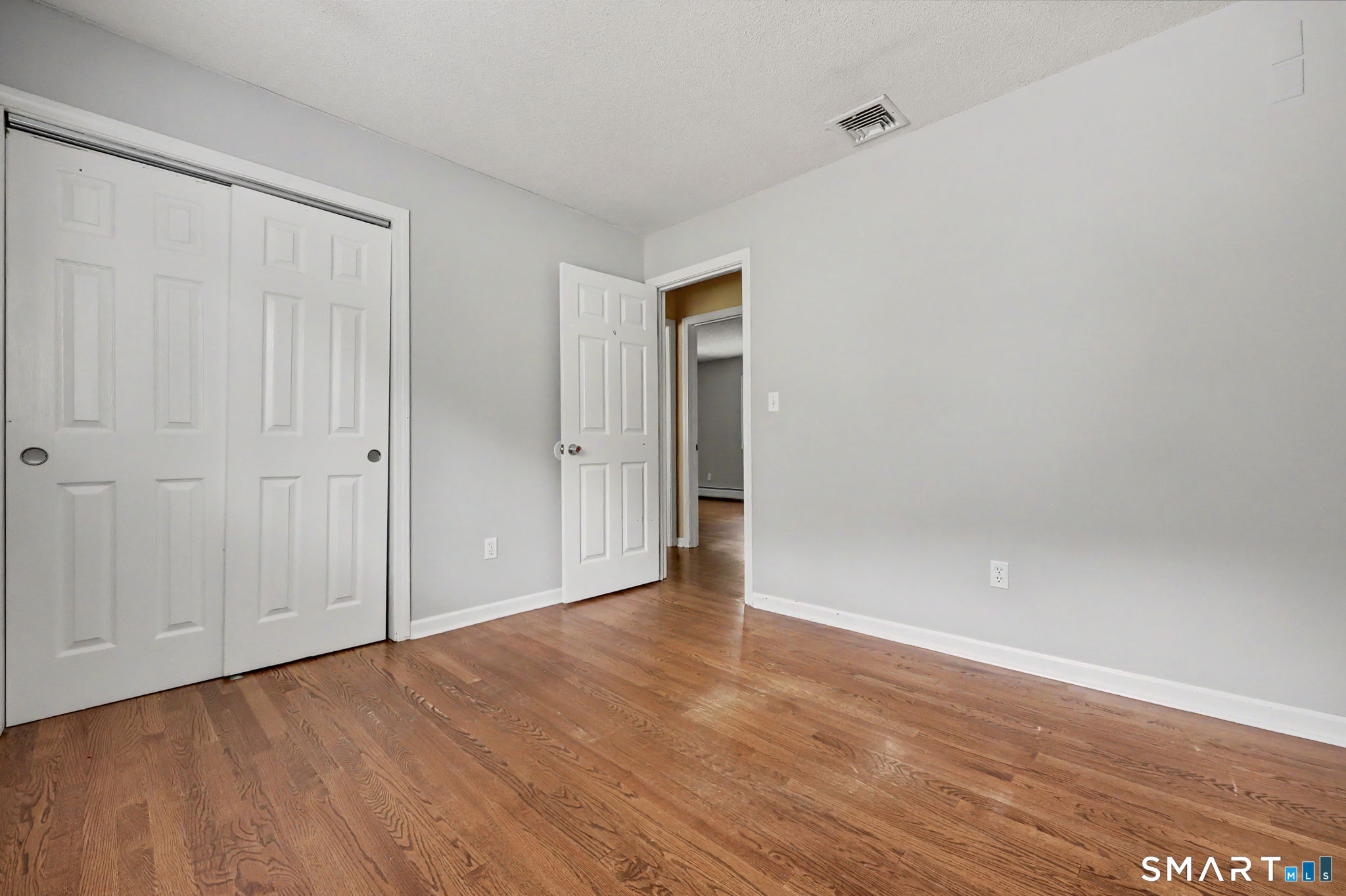 Empty bedroom with hardwood floors, a white sliding-door closet, and an open doorway.