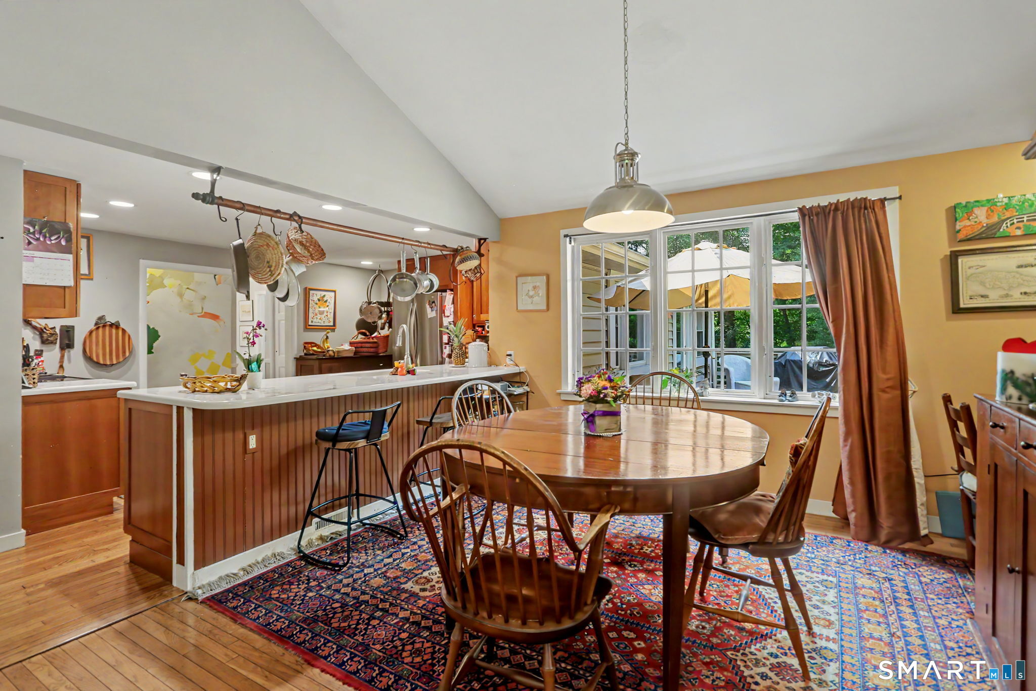 Kitchen and dining area with a white breakfast bar, wooden table, and large patio-facing windows.