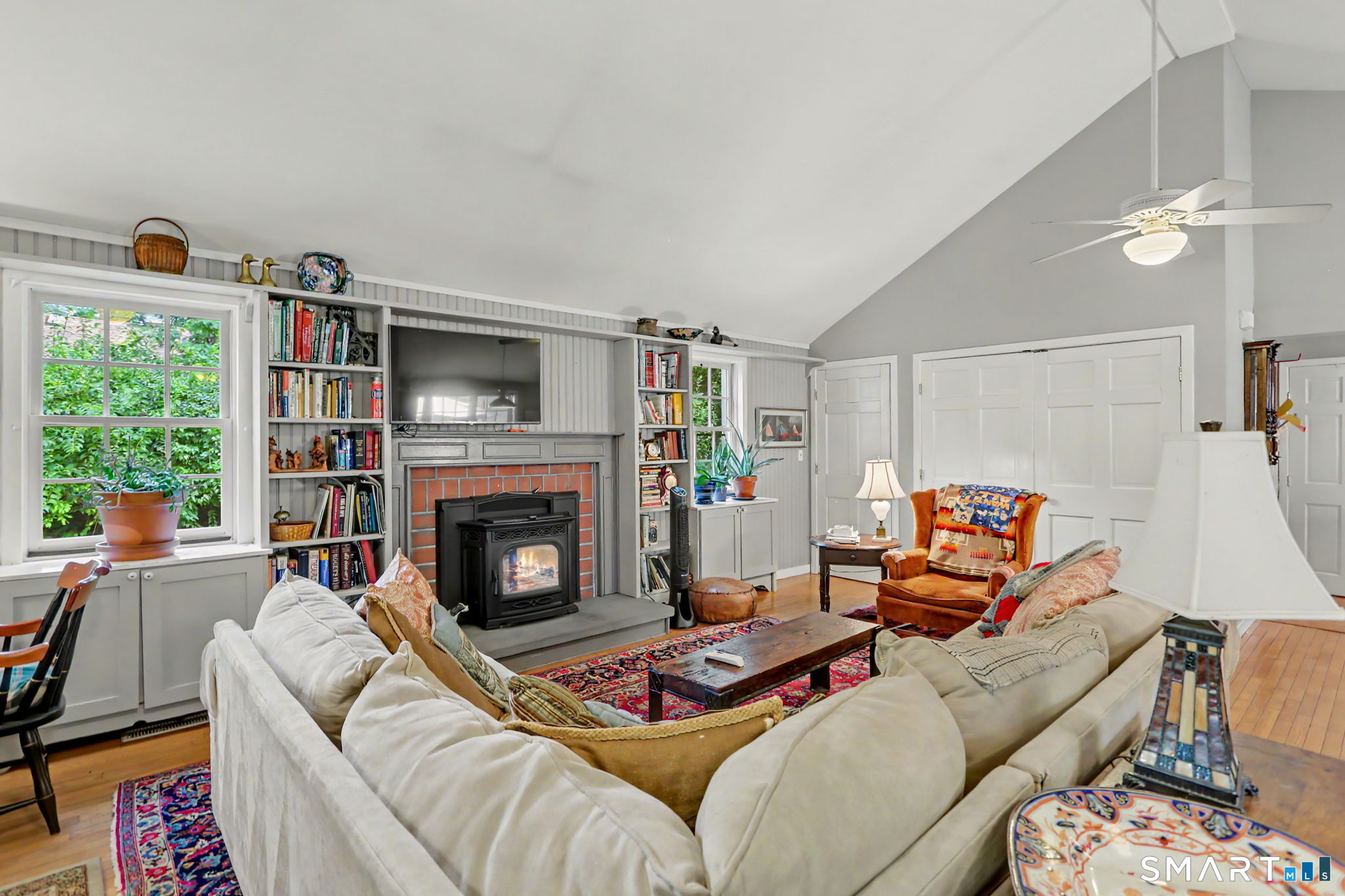 Living room with a vaulted ceiling, built-in bookshelves, and a wood stove in a brick fireplace.