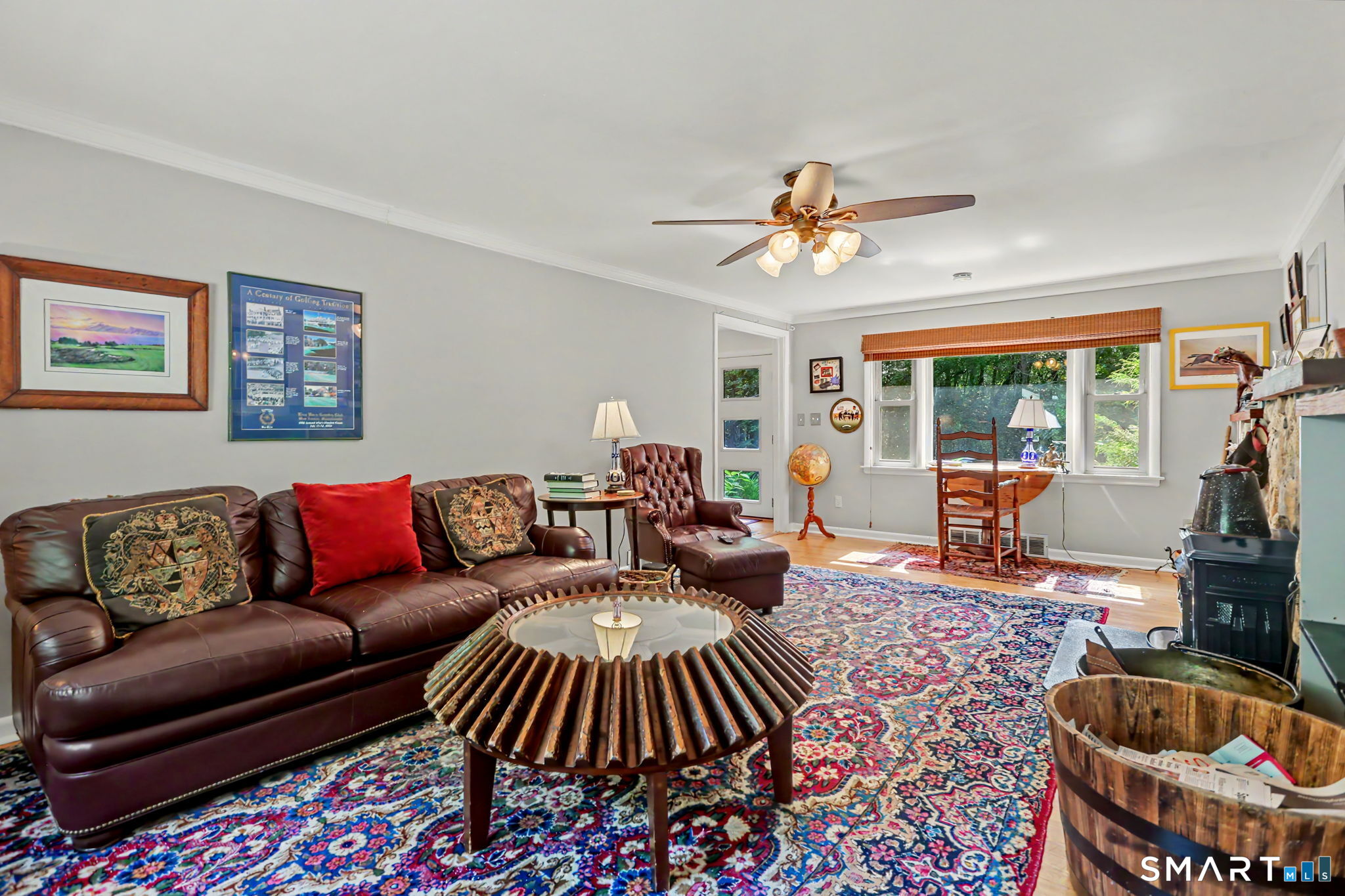 Living room with leather seating, colorful patterned rugs, a broad garden-view window, and a wood-burning stove.