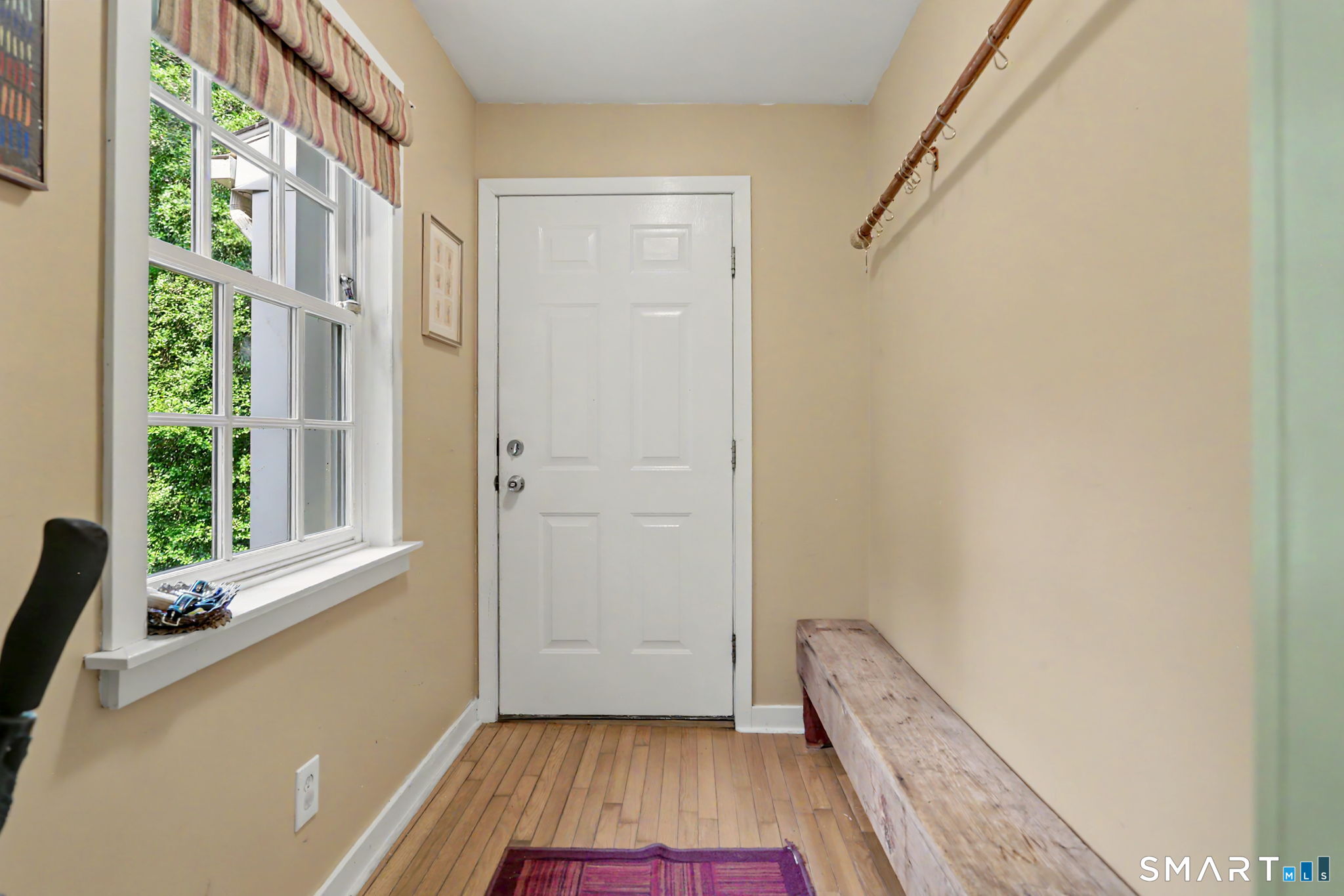 Entryway with a white paneled door, large window, wood floors, and a long bench.