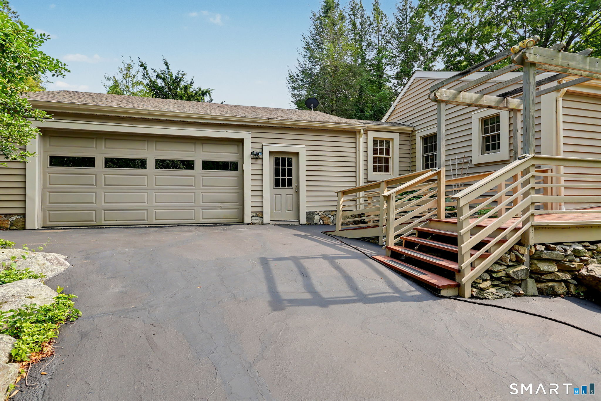 House exterior with a large garage and raised wooden deck and pergola beside the driveway.
