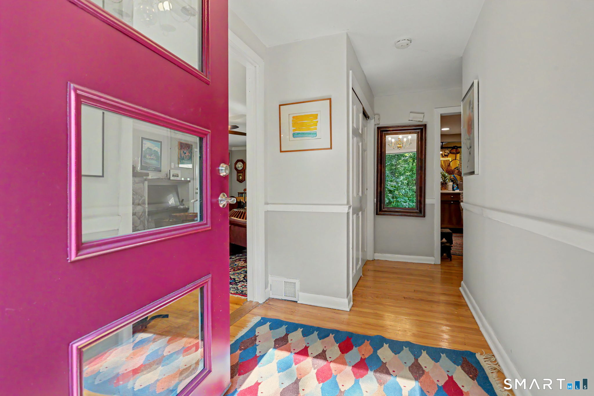 Entry hallway with an open magenta glass-paneled door, hardwood floors, and a colorful geometric rug.