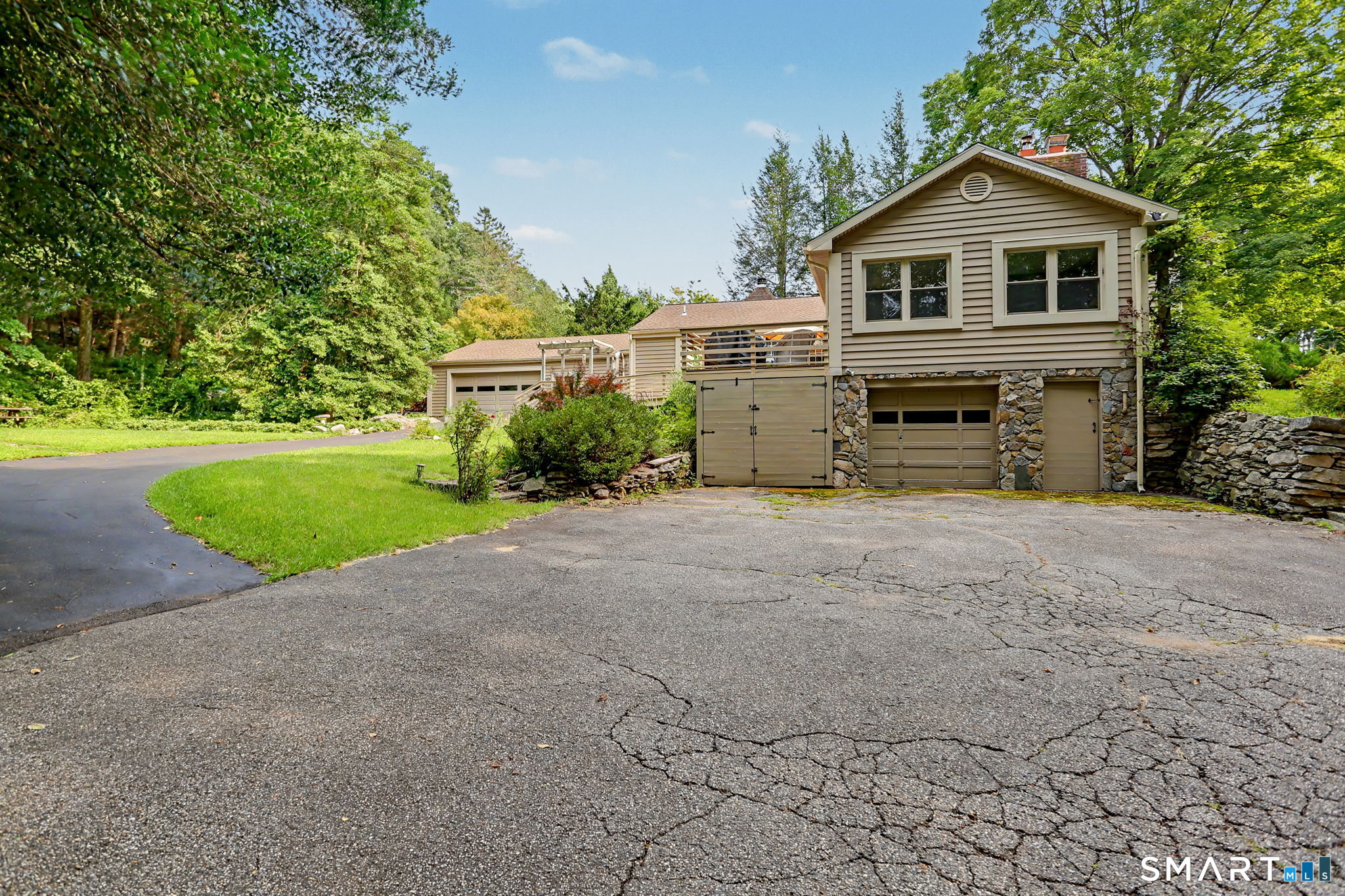 Beige split-level home with stone garage accents, broad driveway, and mature trees.