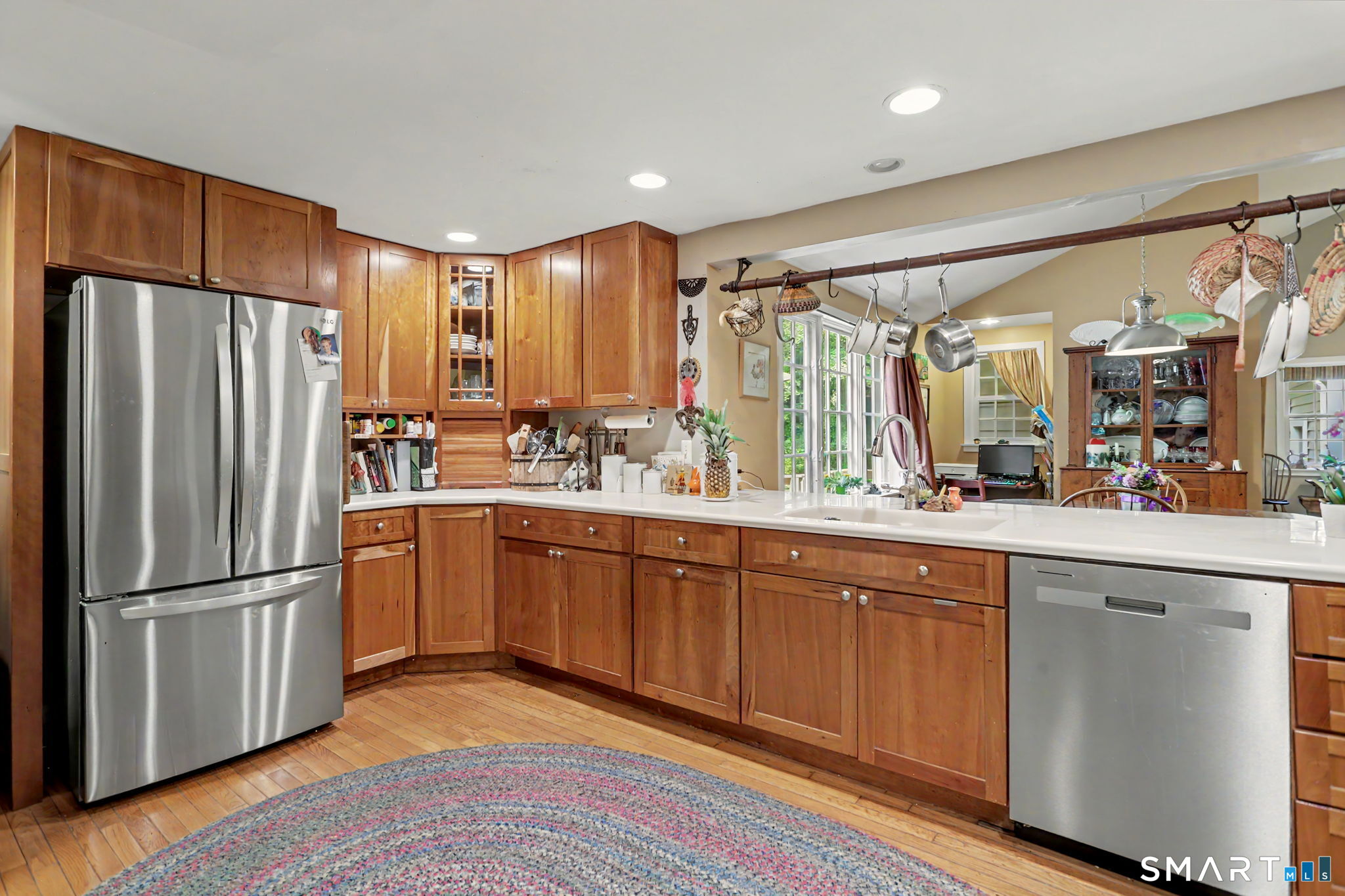 Kitchen with wood cabinetry, stainless appliances, white counters, and an overhead pot rack.