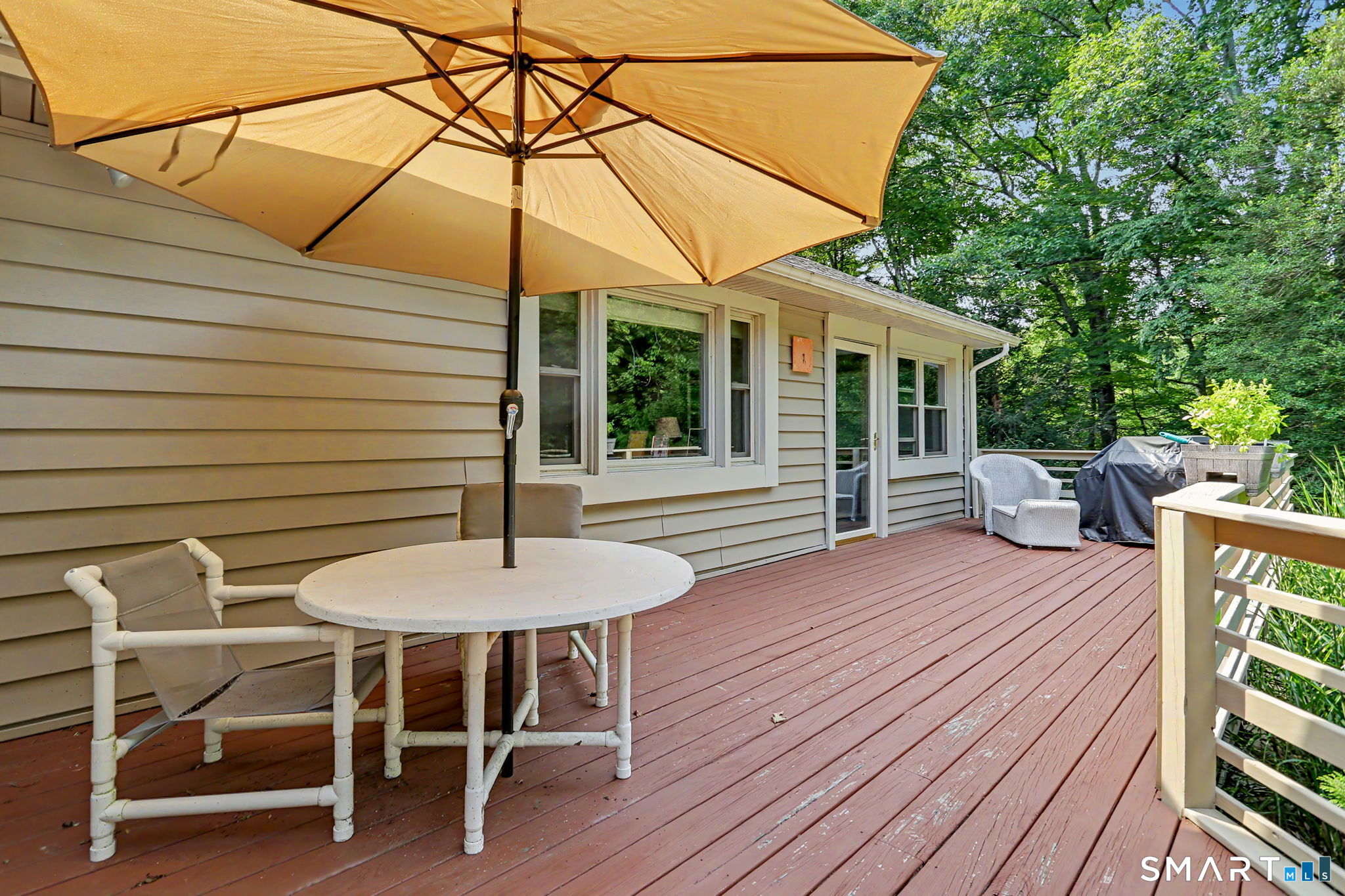 House deck with a large tan umbrella shading a round table and patio chairs.