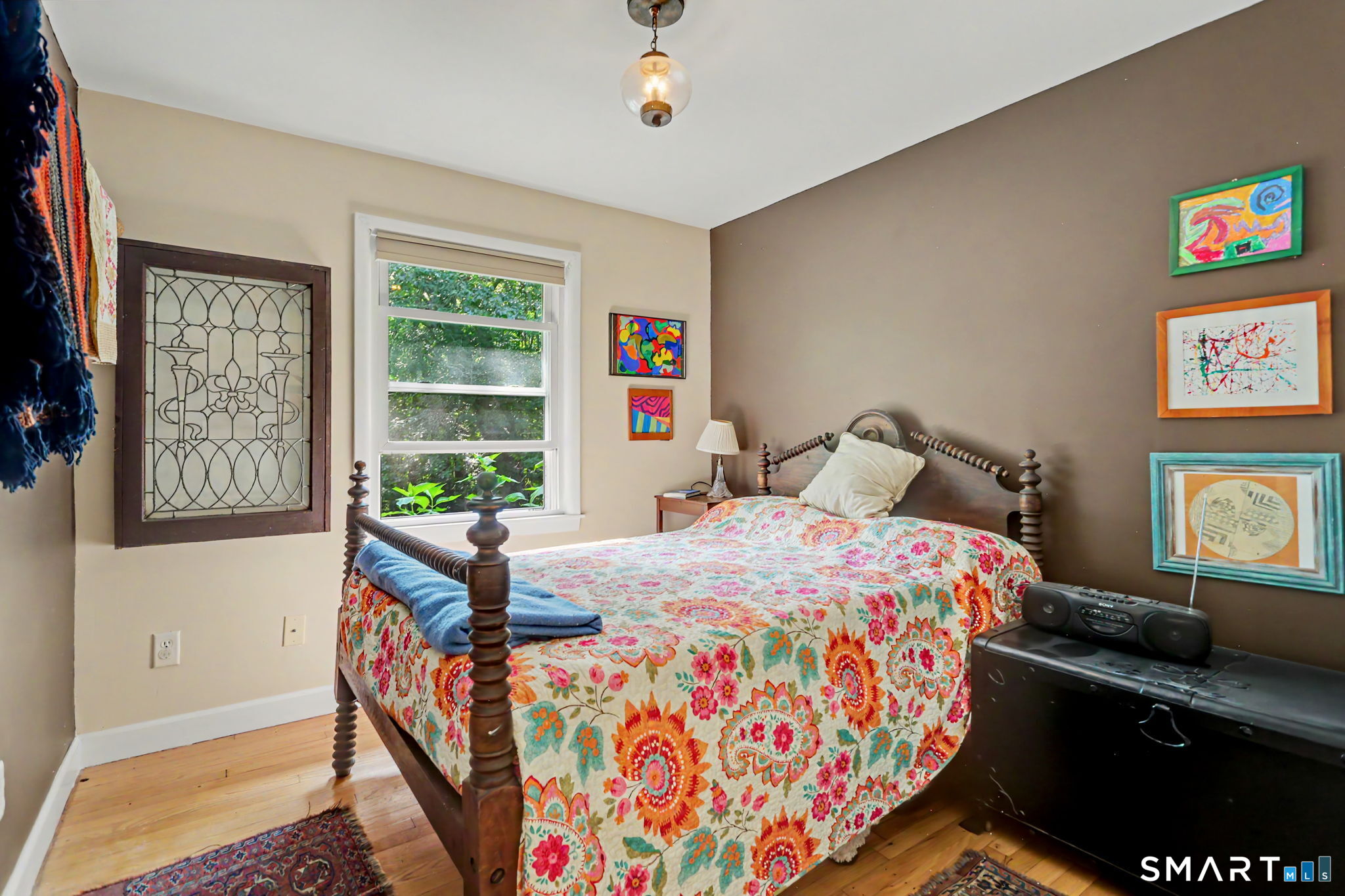Bedroom with a dark four-poster bed, bright floral bedding, hardwood floors, and colorful framed artwork.