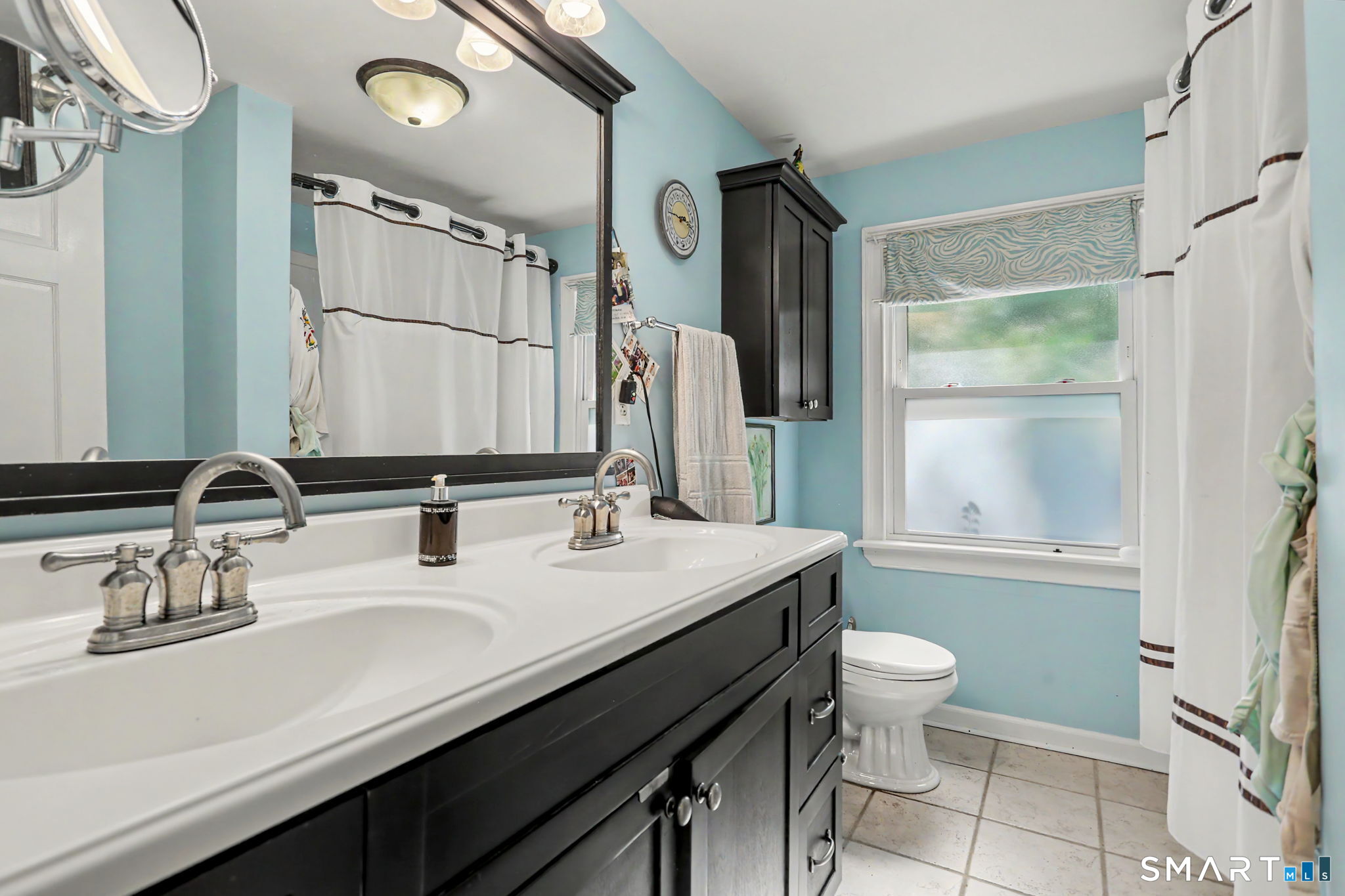 Bathroom with dark double-sink vanity, aqua walls, and a window beside the toilet.