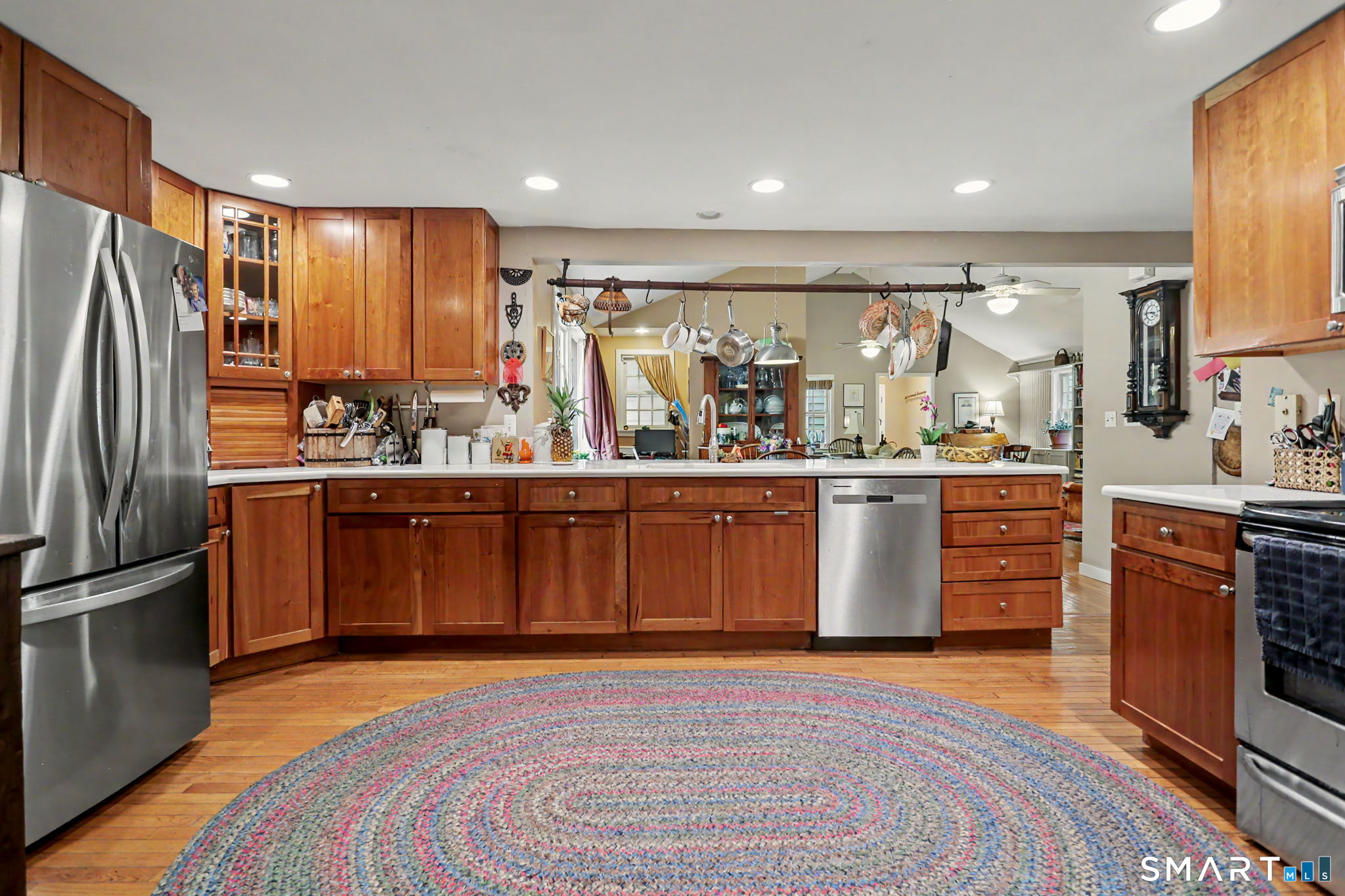 Open kitchen with warm wood cabinetry, stainless appliances, and a ceiling rack hung with pots.
