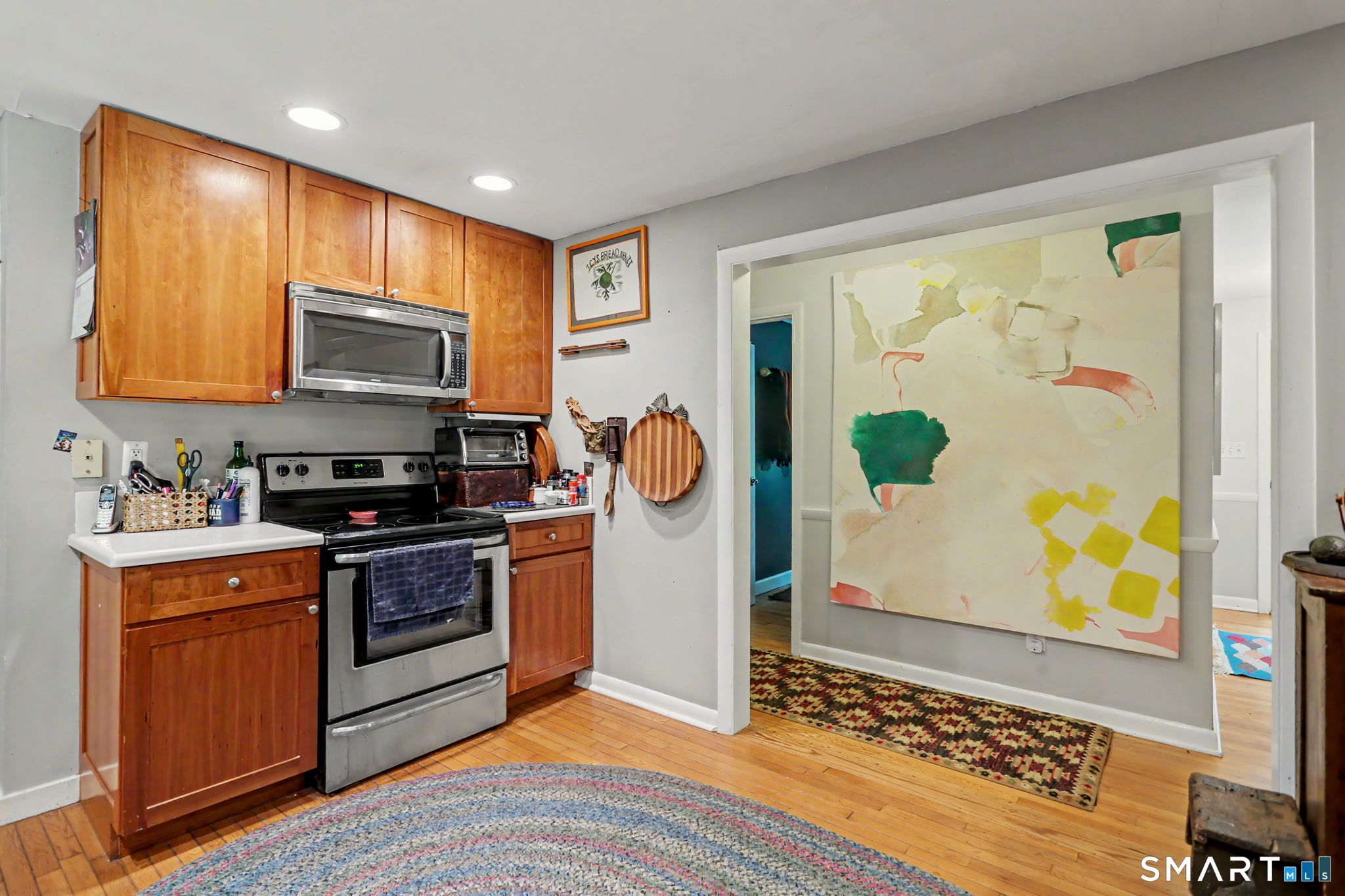 Kitchen with wood cabinets, stainless steel appliances, hardwood floors, and a large abstract painting in the adjoining doorway.