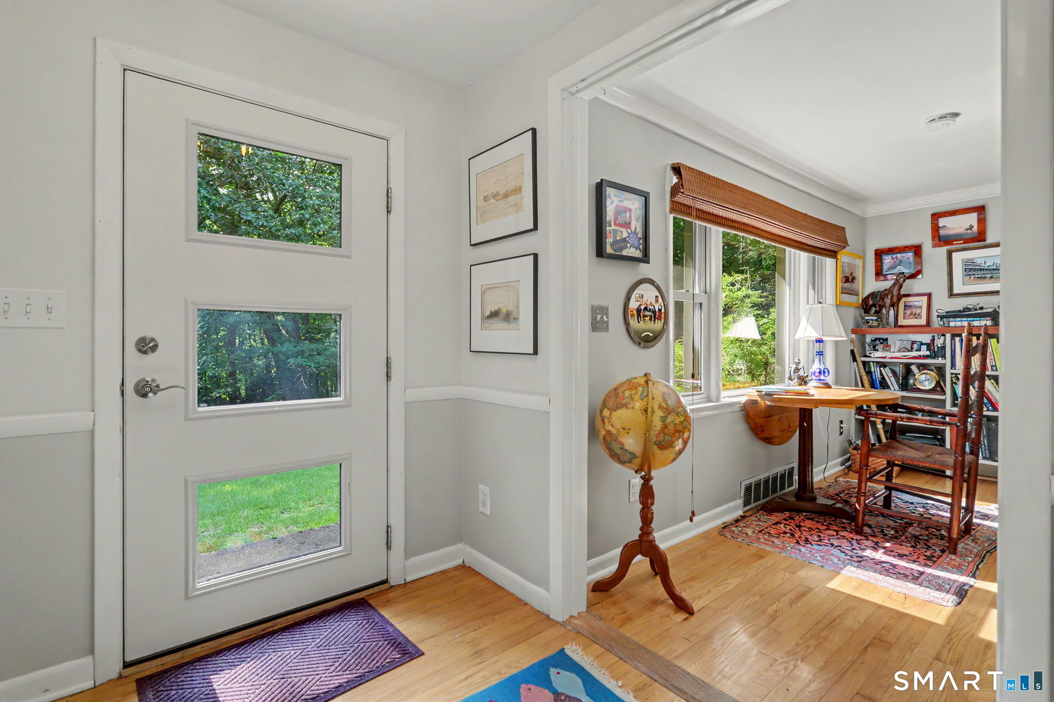 Bright entryway with a three-window front door and hardwood floors opening to a furnished study.