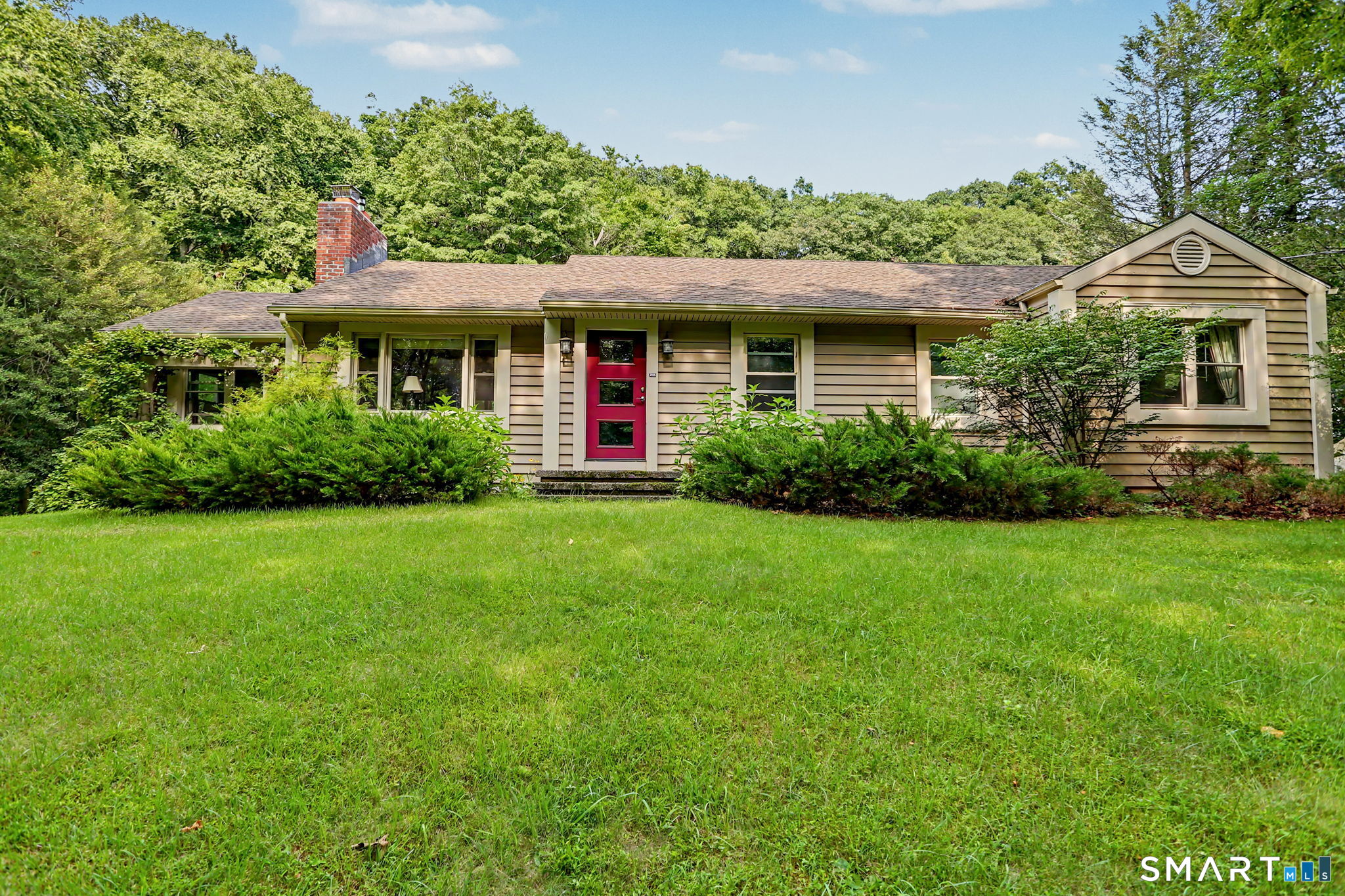 Single-story home with beige siding, a red front door, brick chimney, and broad green lawn.