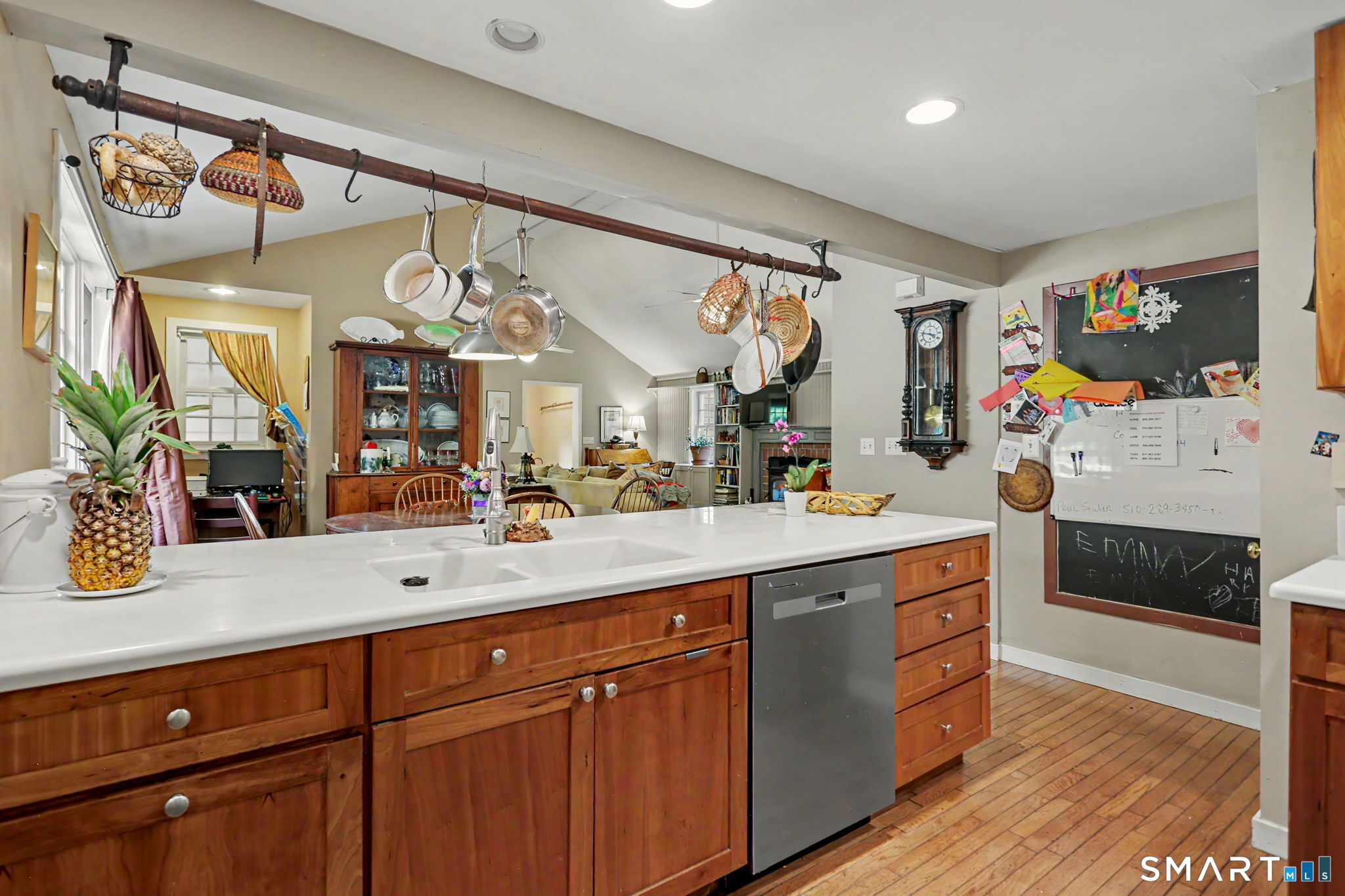 Kitchen with wood cabinetry, white island, hanging cookware, and an open view into the living area.