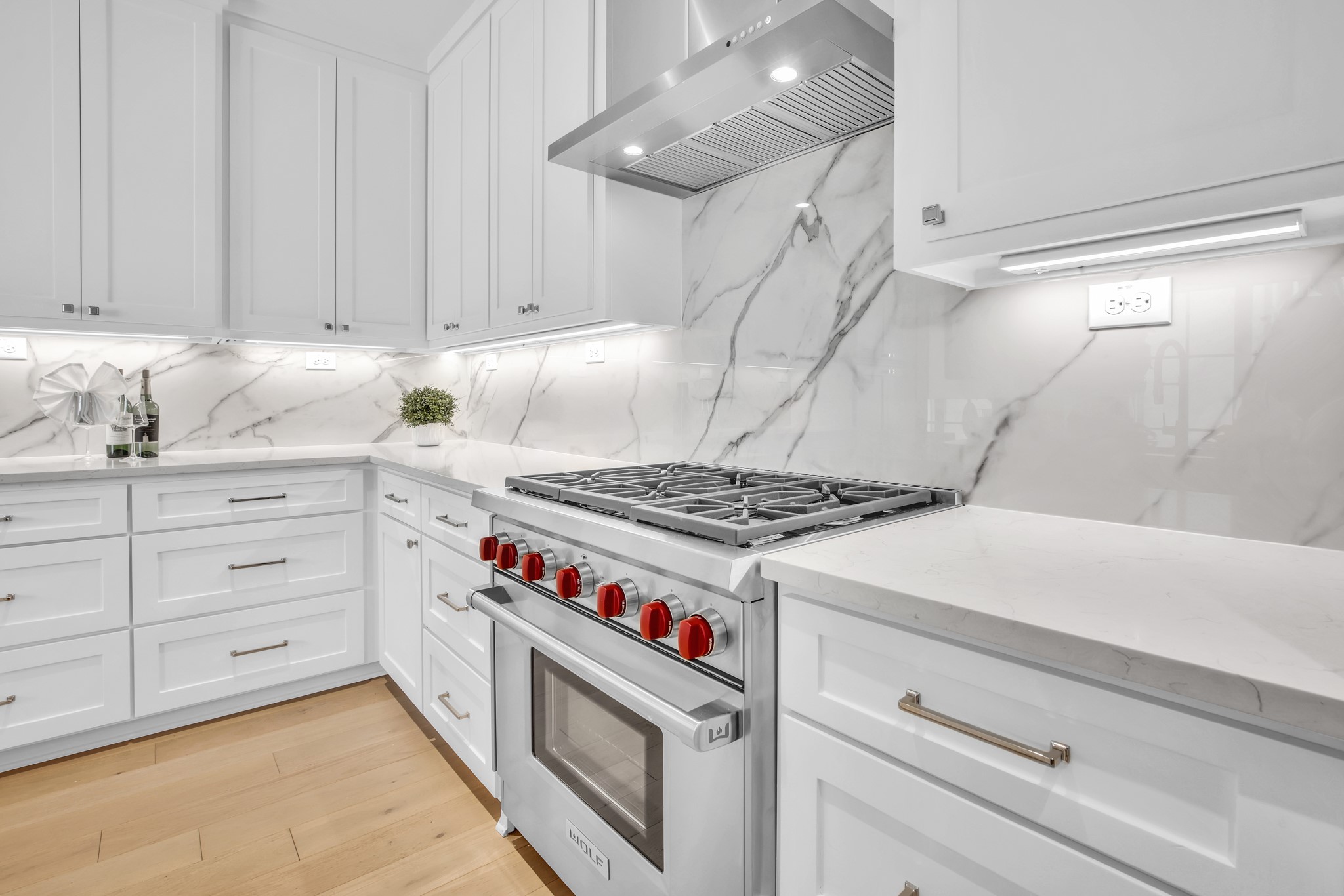 White kitchen with marble counters and backsplash, featuring a stainless steel range with red knobs.