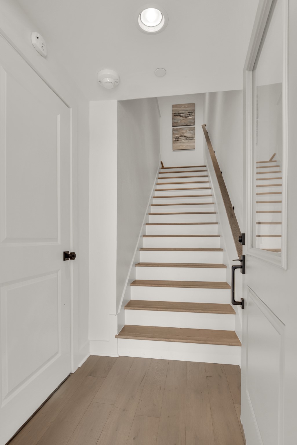 Staircase with light wood treads, white risers, a dark handrail, and artwork above.