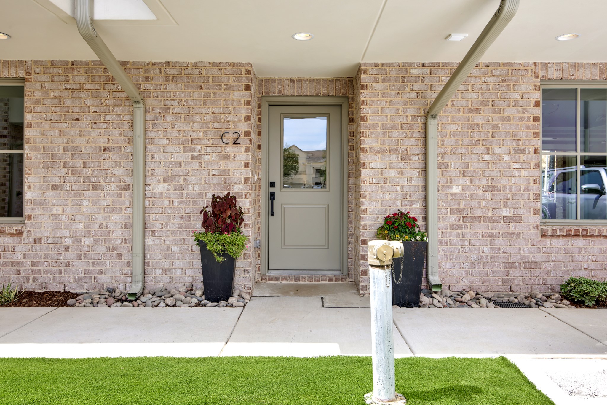 Brick building entrance with a recessed gray door marked C2 and flower planters.