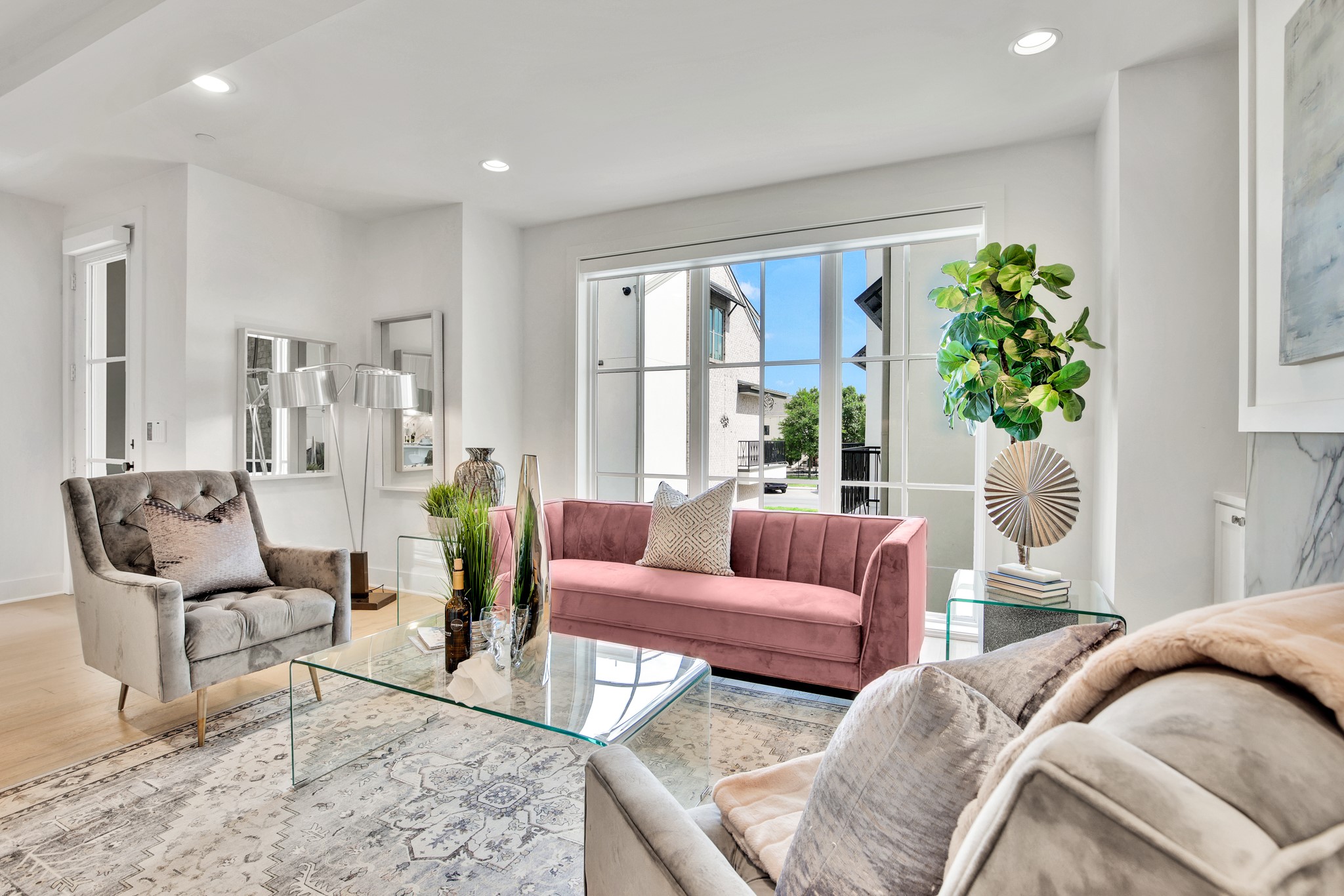 Living room with a pink sofa, gray armchairs, glass coffee table, and large windows.