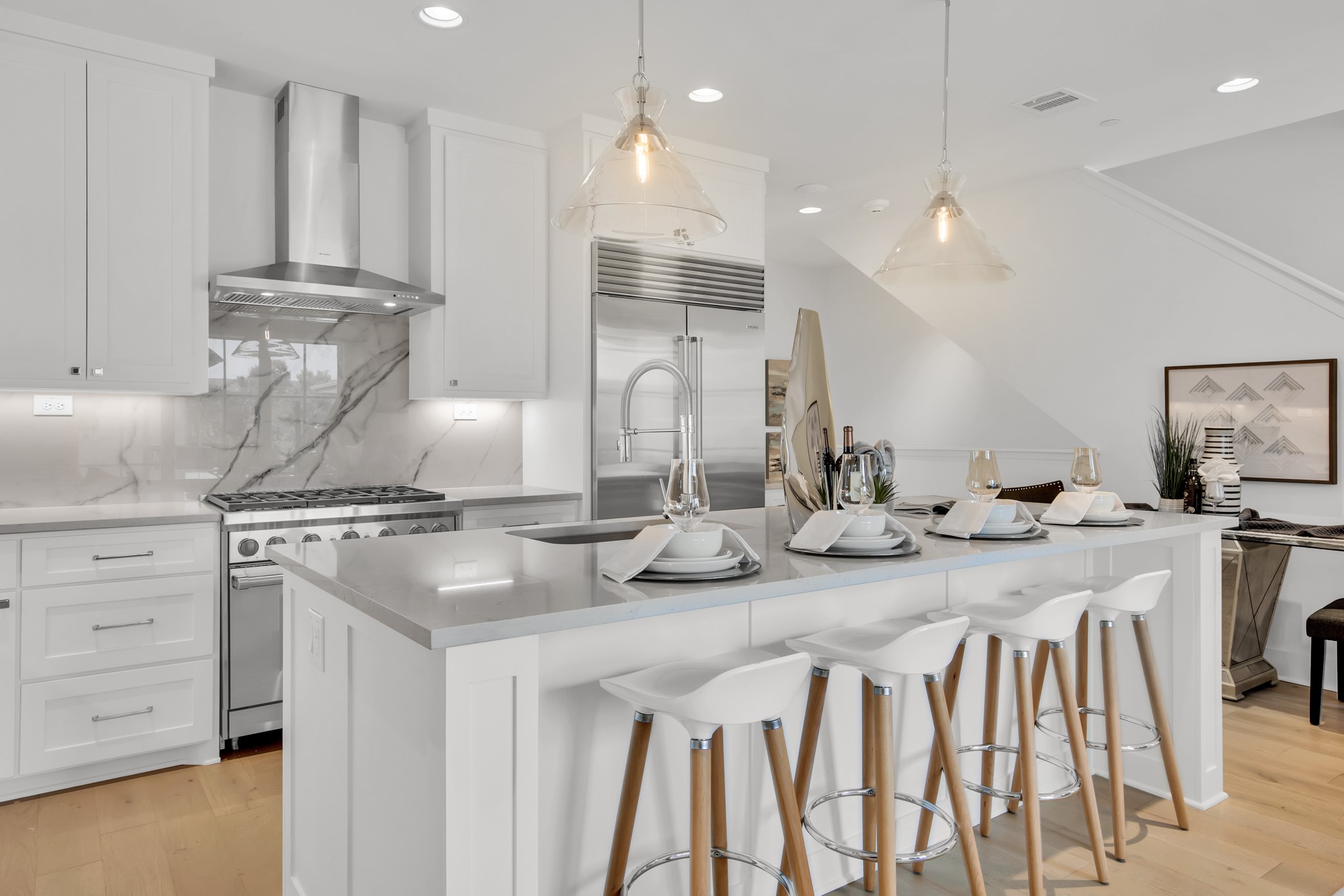 Bright white kitchen with marble-veined backsplash, stainless appliances, and a large island with bar stools.