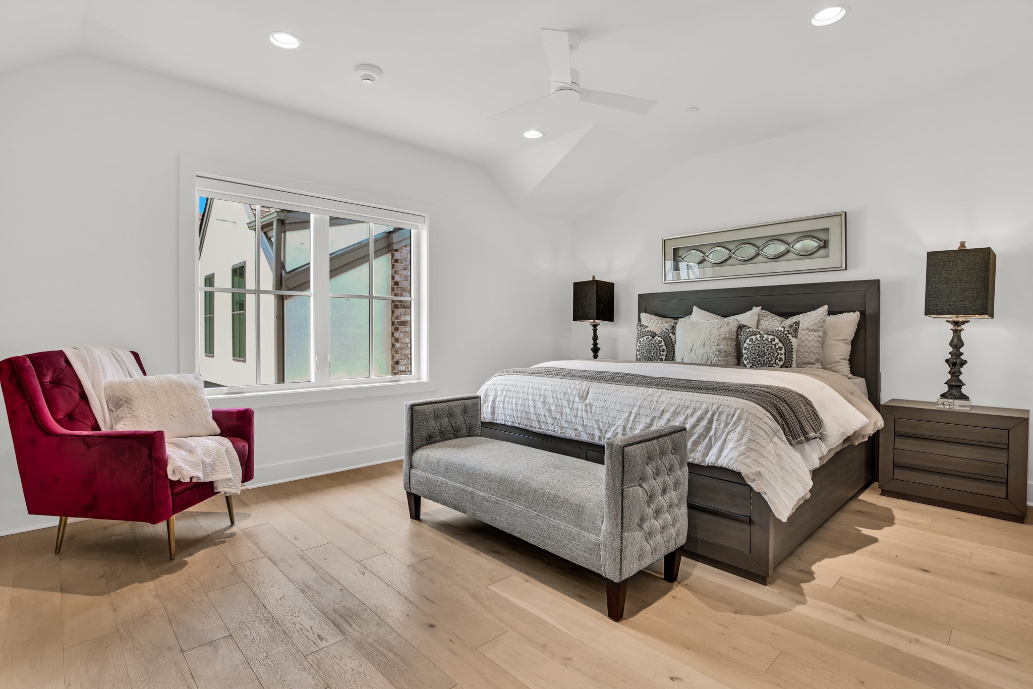 Furnished bedroom with a dark wood bed, gray bench, and burgundy accent chair.
