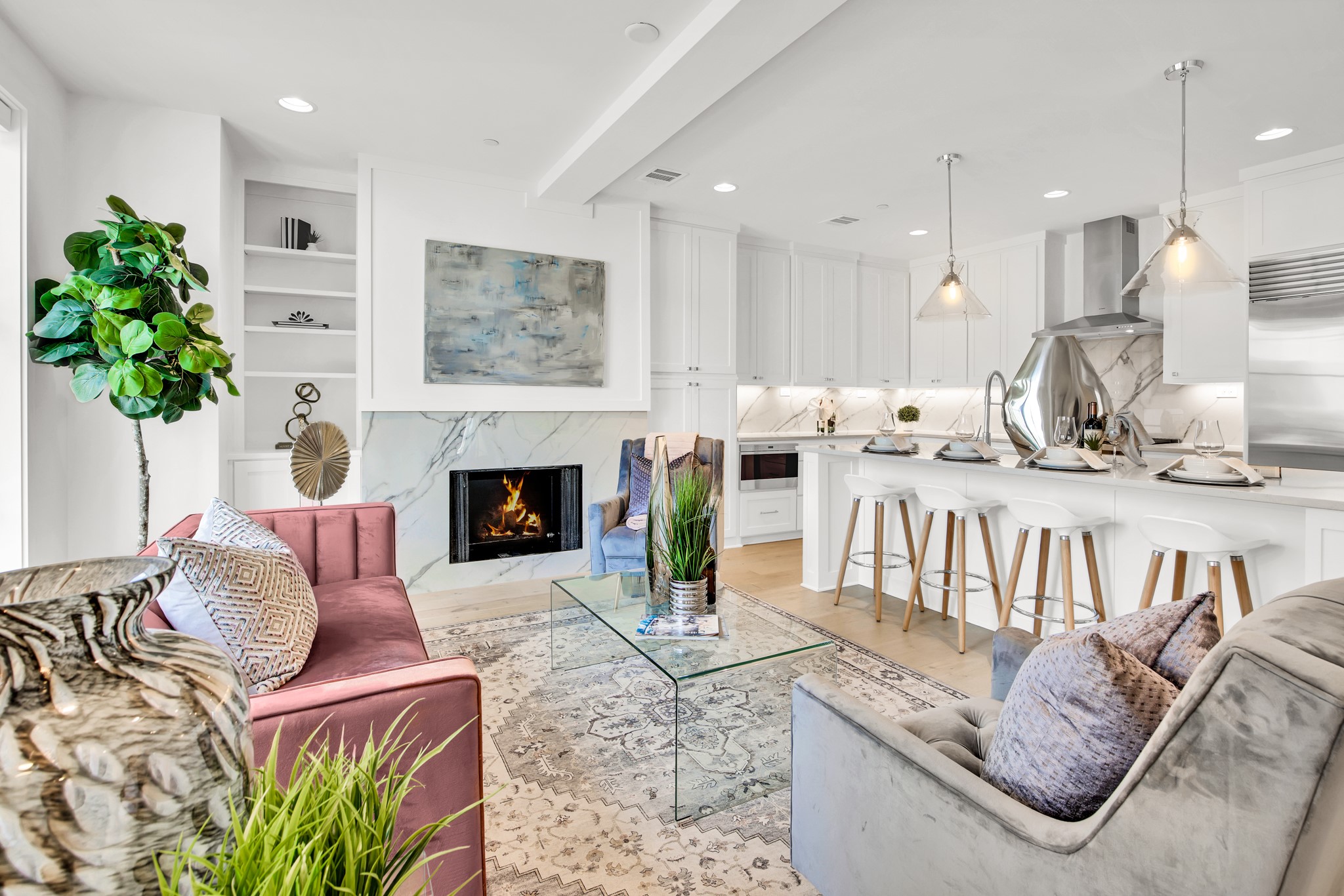 Open-plan living room and kitchen with a marble fireplace wall and a large island lined with bar stools.