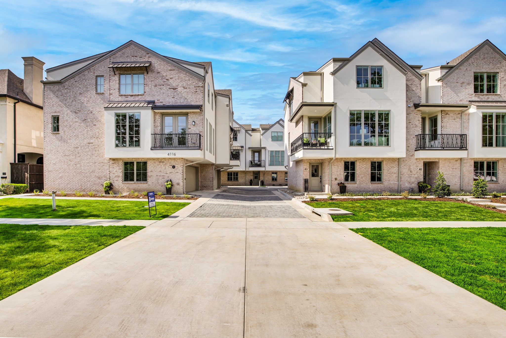 Attached townhomes with pale brick façades, balconies, and a landscaped shared driveway.