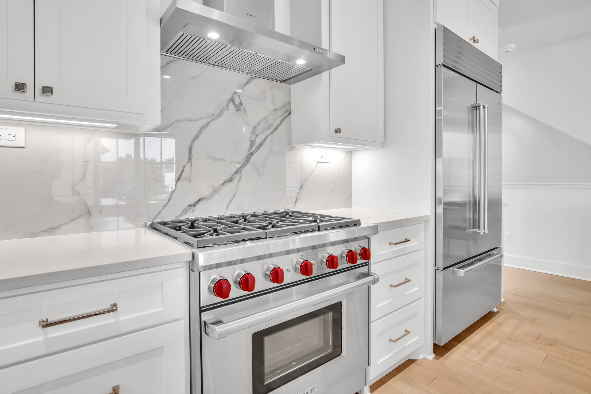 Modern white kitchen with a veined marble backsplash and stainless steel range with red knobs.