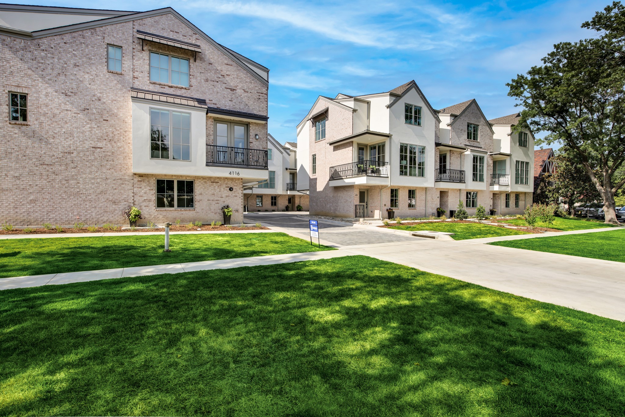 Modern multi-story townhomes with pale brick façades, black balconies, and landscaped front lawns.