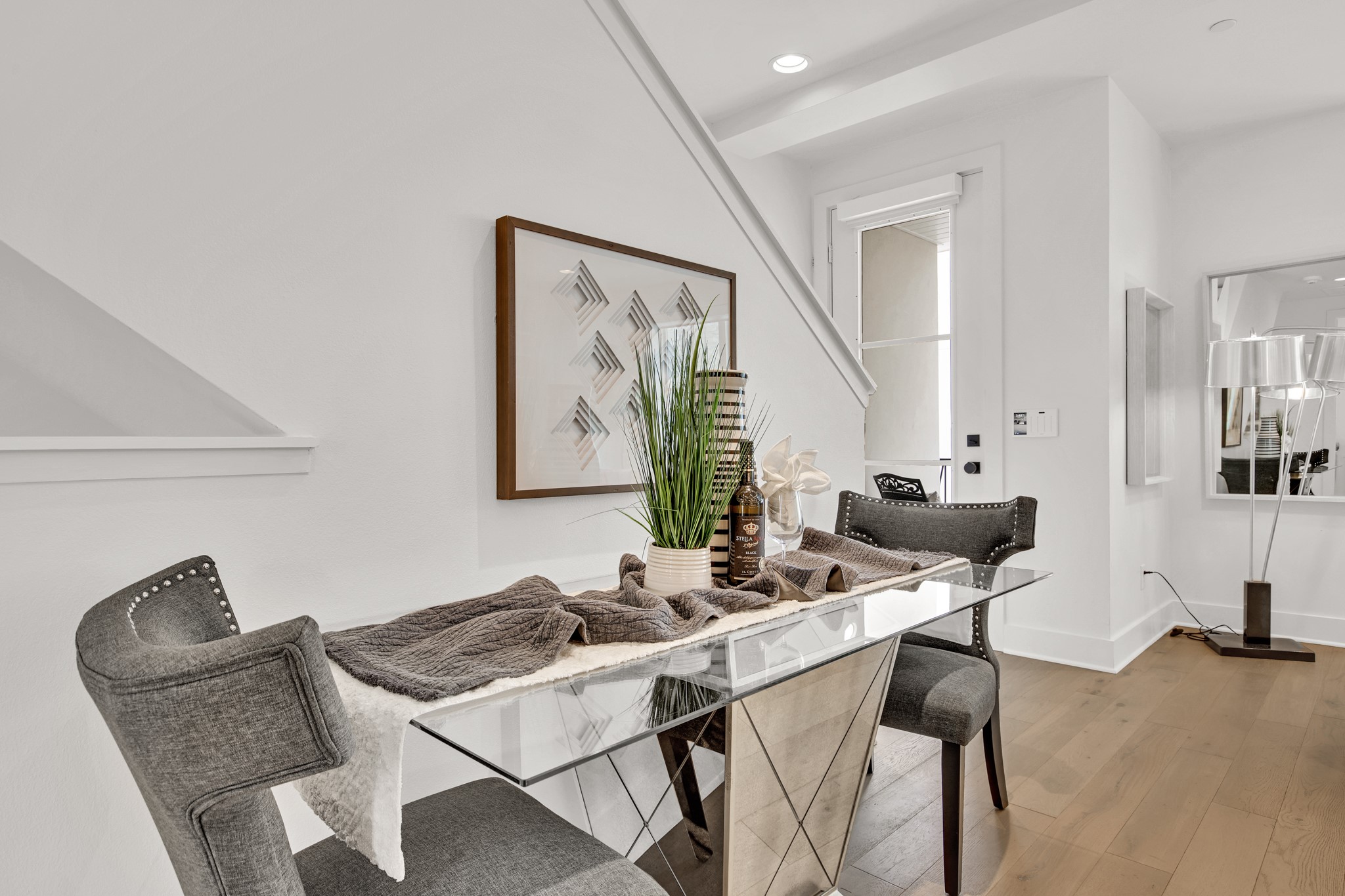 Dining area with a glass-top table, gray chairs, and framed geometric artwork.