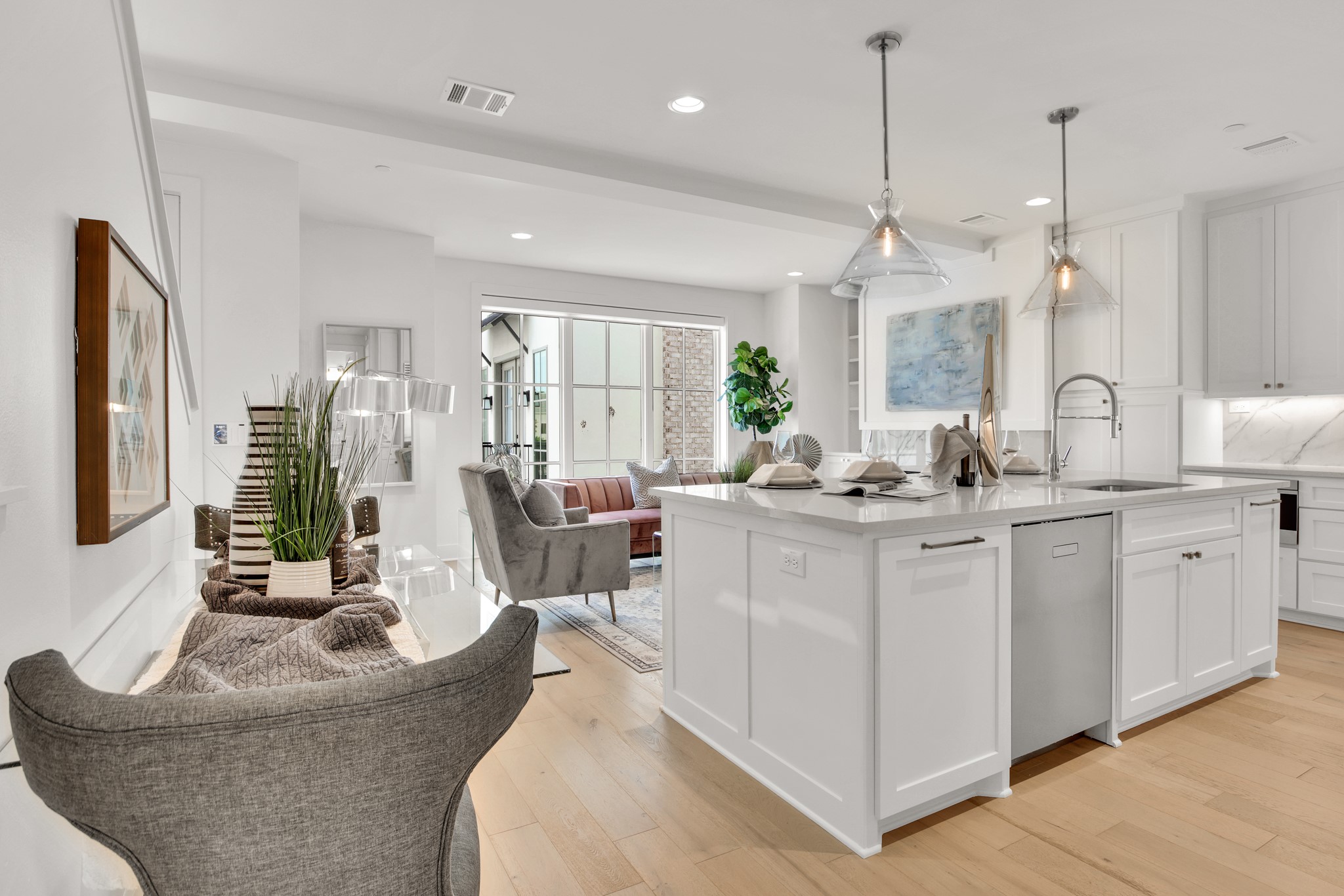 Staged open-plan kitchen and living area with a large white island and glass pendant lights.