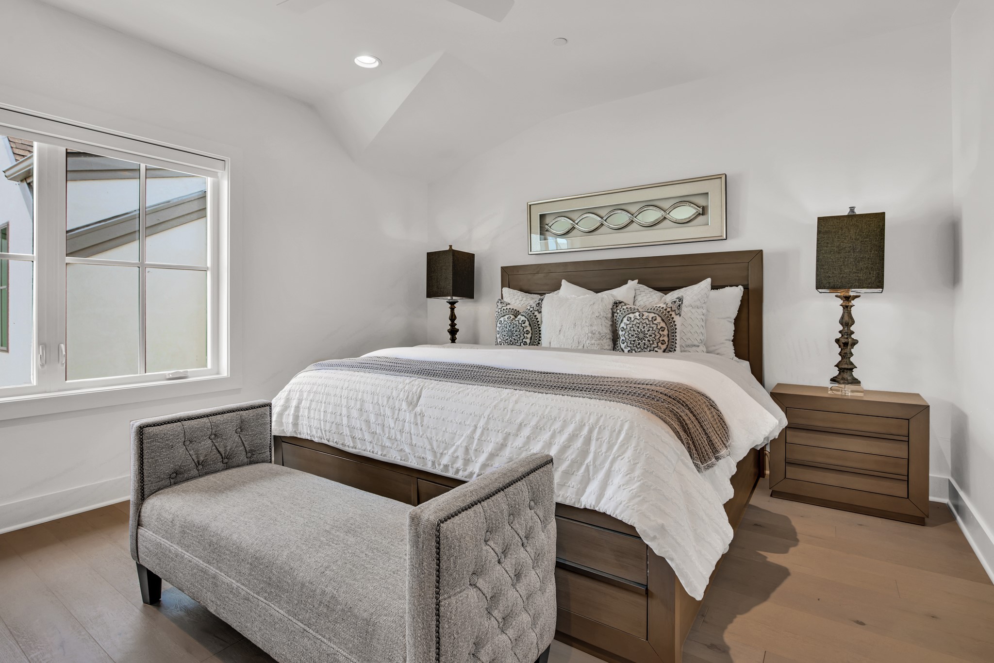 Furnished bedroom with a wood-framed bed, gray bench, and large window.