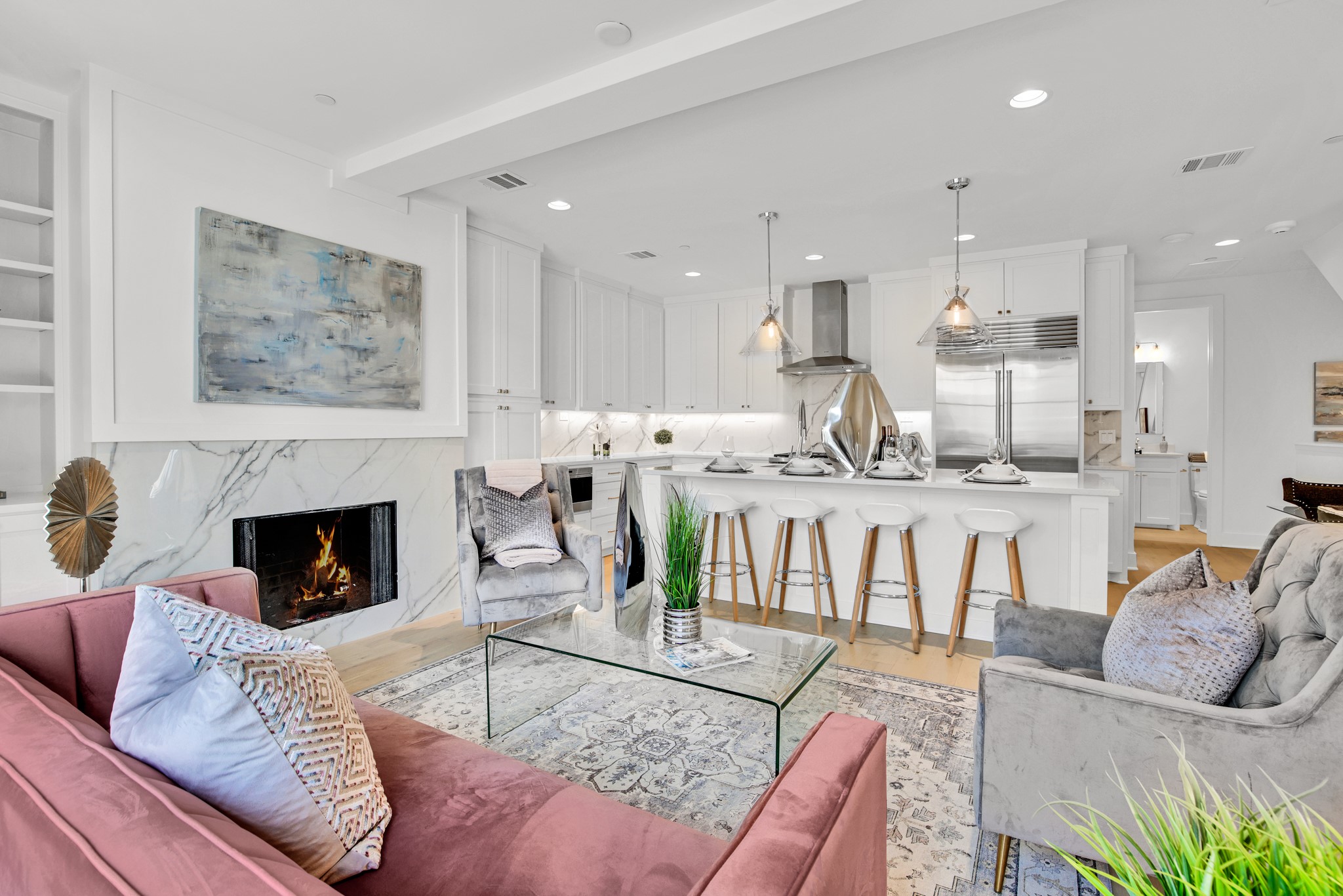 Open-plan living room and kitchen with a marble fireplace, pink sofa, and white island.