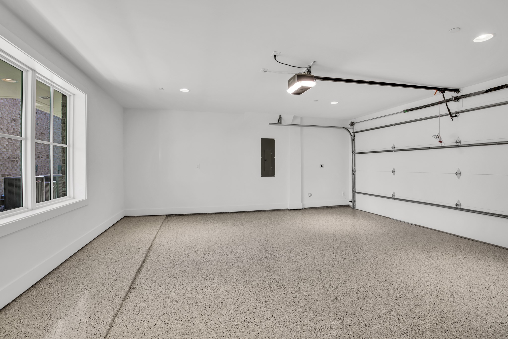 Empty garage with a speckled floor, large window, and white overhead door.