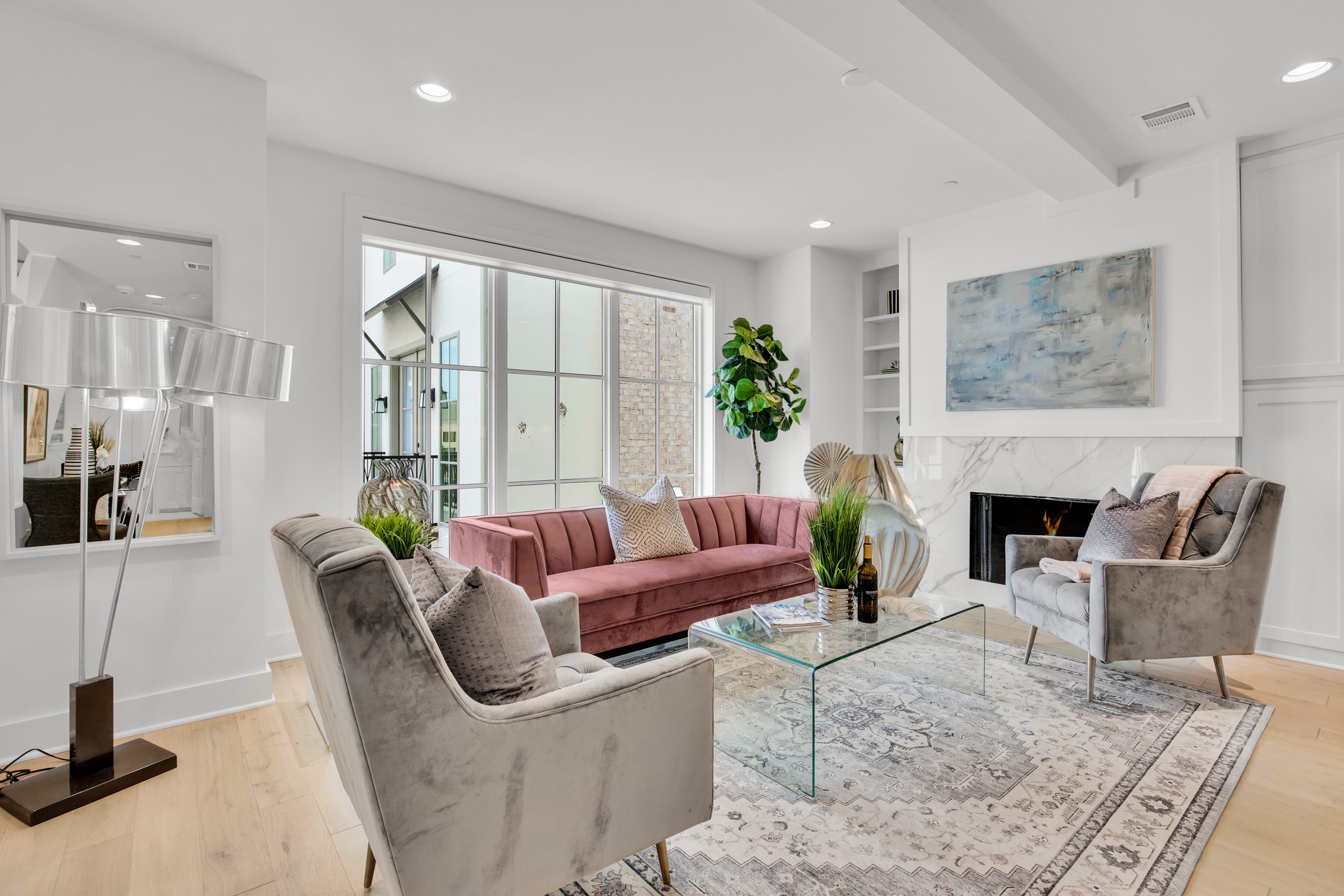 Staged living room with a pink sofa, large windows, and a marble-surround fireplace.