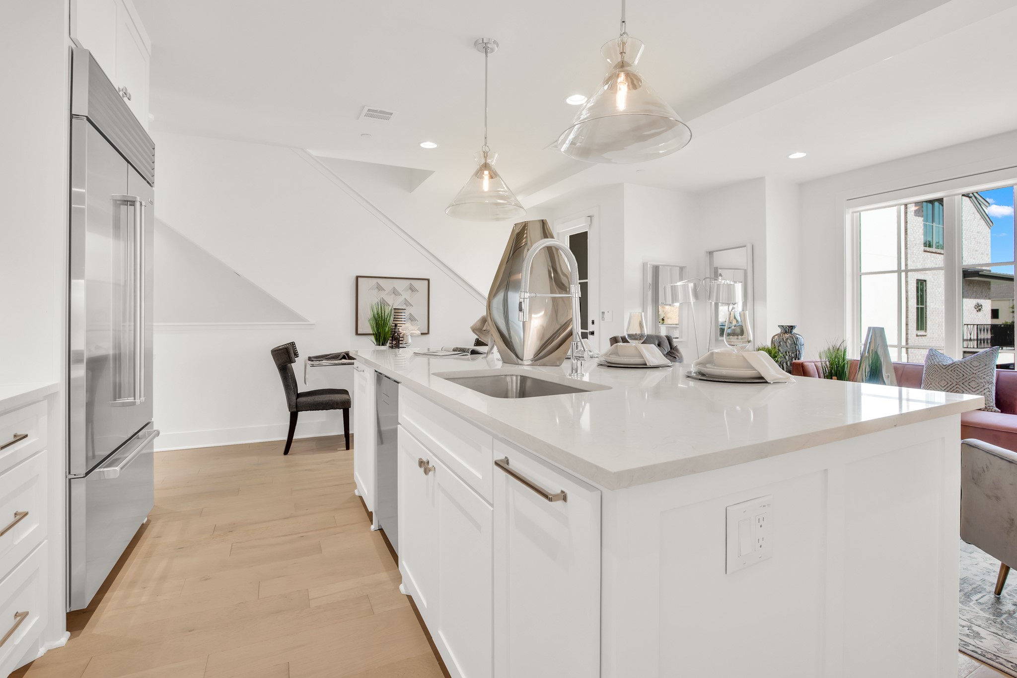 Bright modern kitchen with a large white island and pendant lights, opening to a dining and living area.