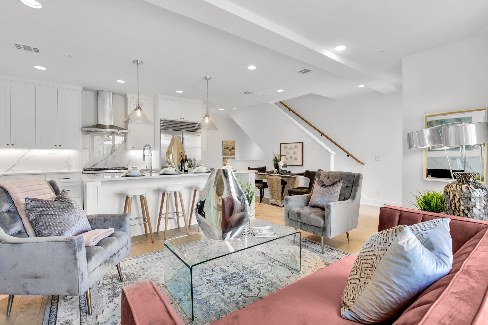Open-plan living room and kitchen with white cabinetry, blush sofa, glass coffee table, and staircase.