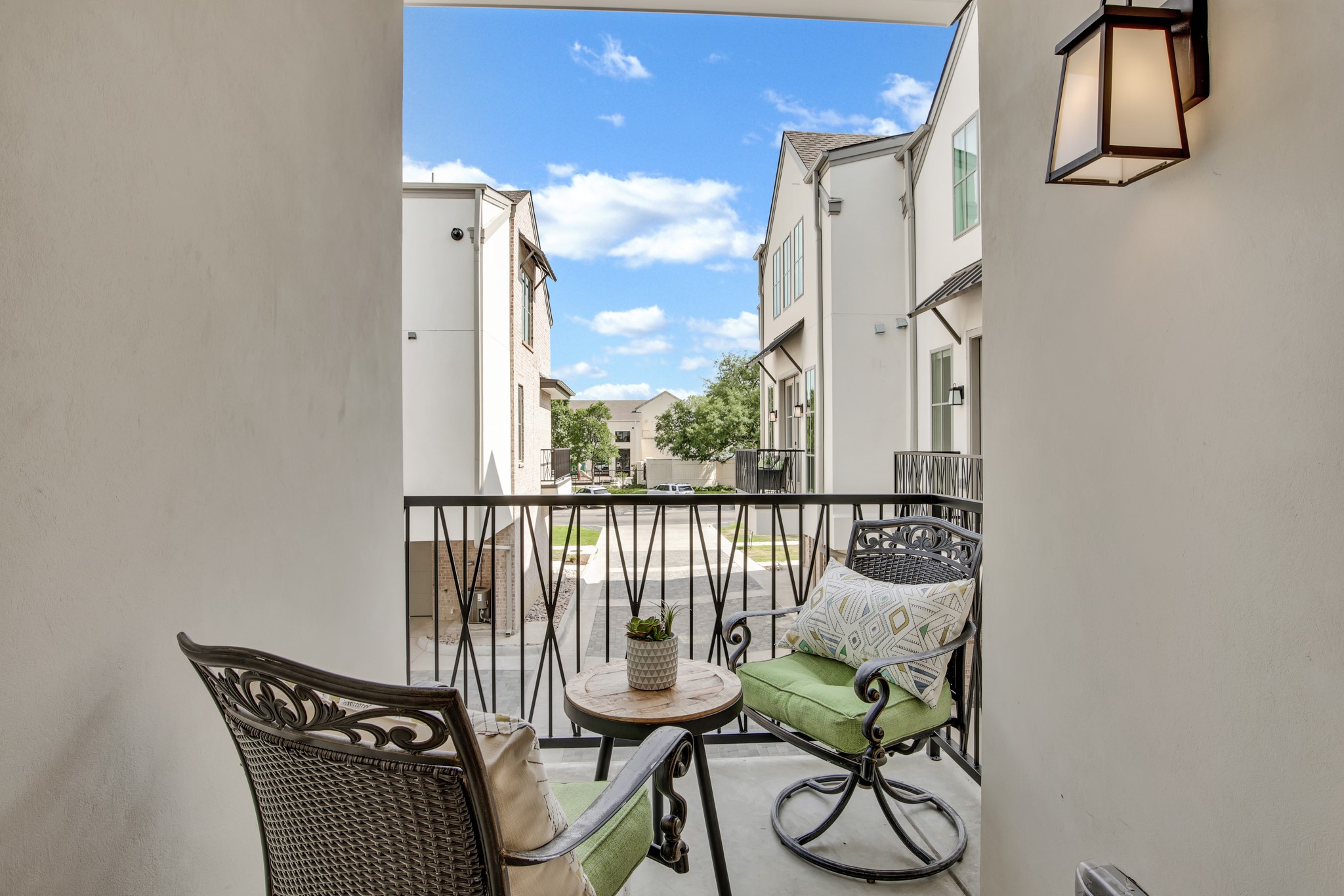 Furnished balcony overlooking a townhome courtyard, with wrought-iron chairs and a small round table.