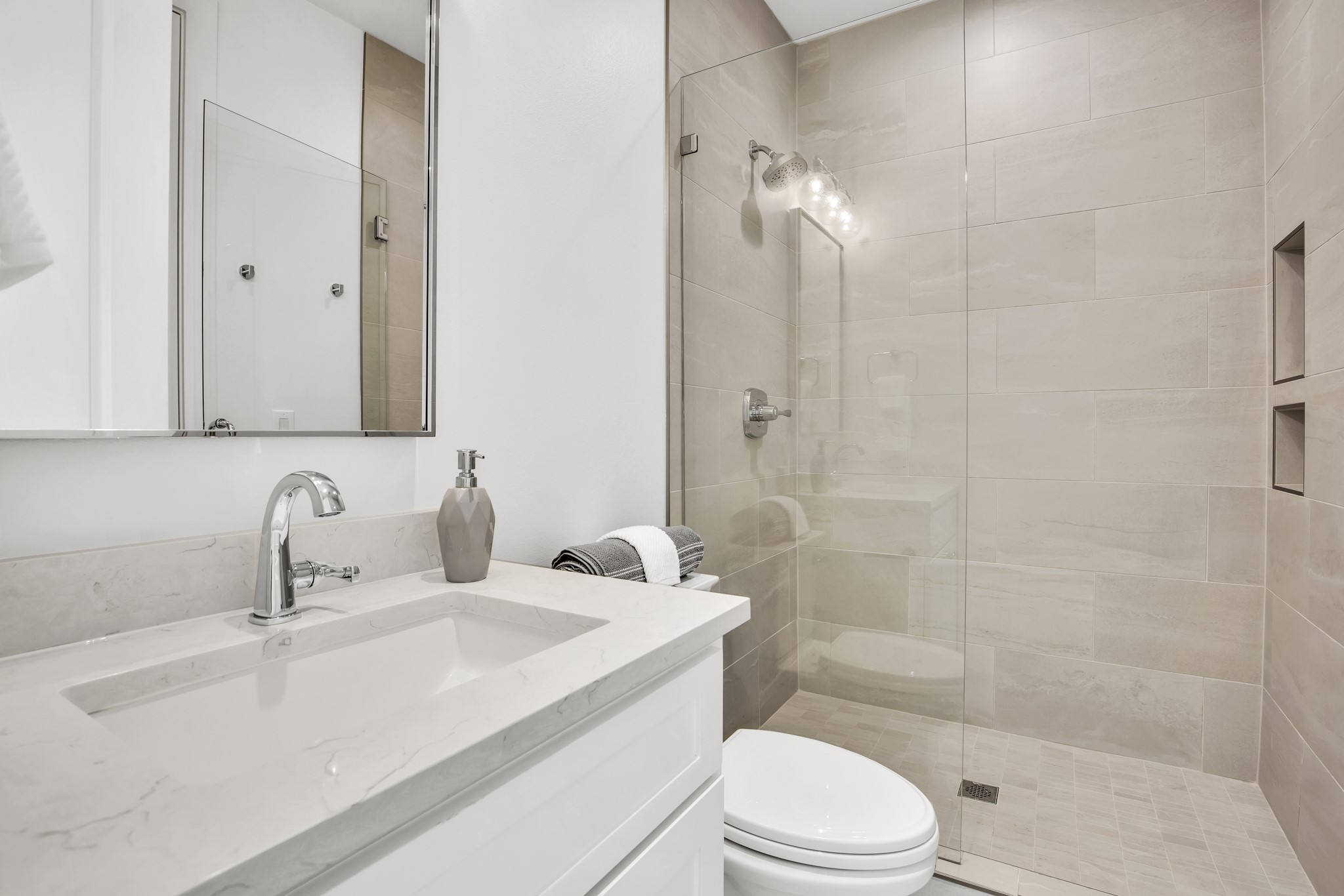 Modern bathroom with a marble vanity and glass walk-in shower with tiled walls and recessed niches.