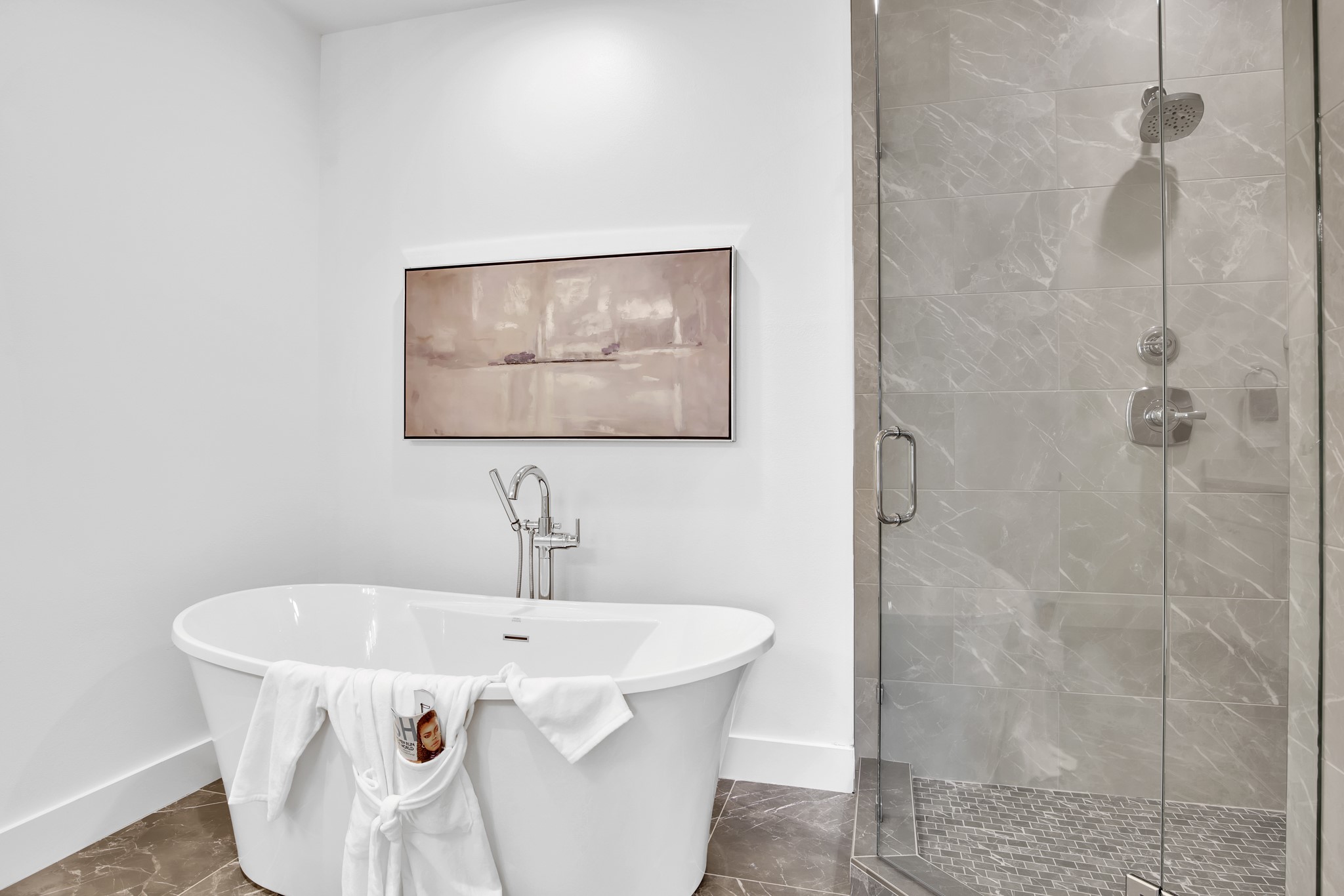 Modern bathroom with a freestanding tub, glass shower, gray tile, and a white robe draped over the tub.