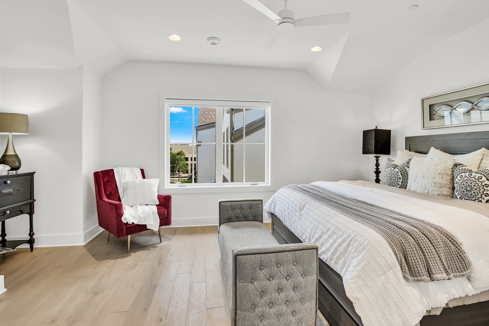 Furnished bedroom with a large bed, red armchair, gray bench, and light wood flooring.