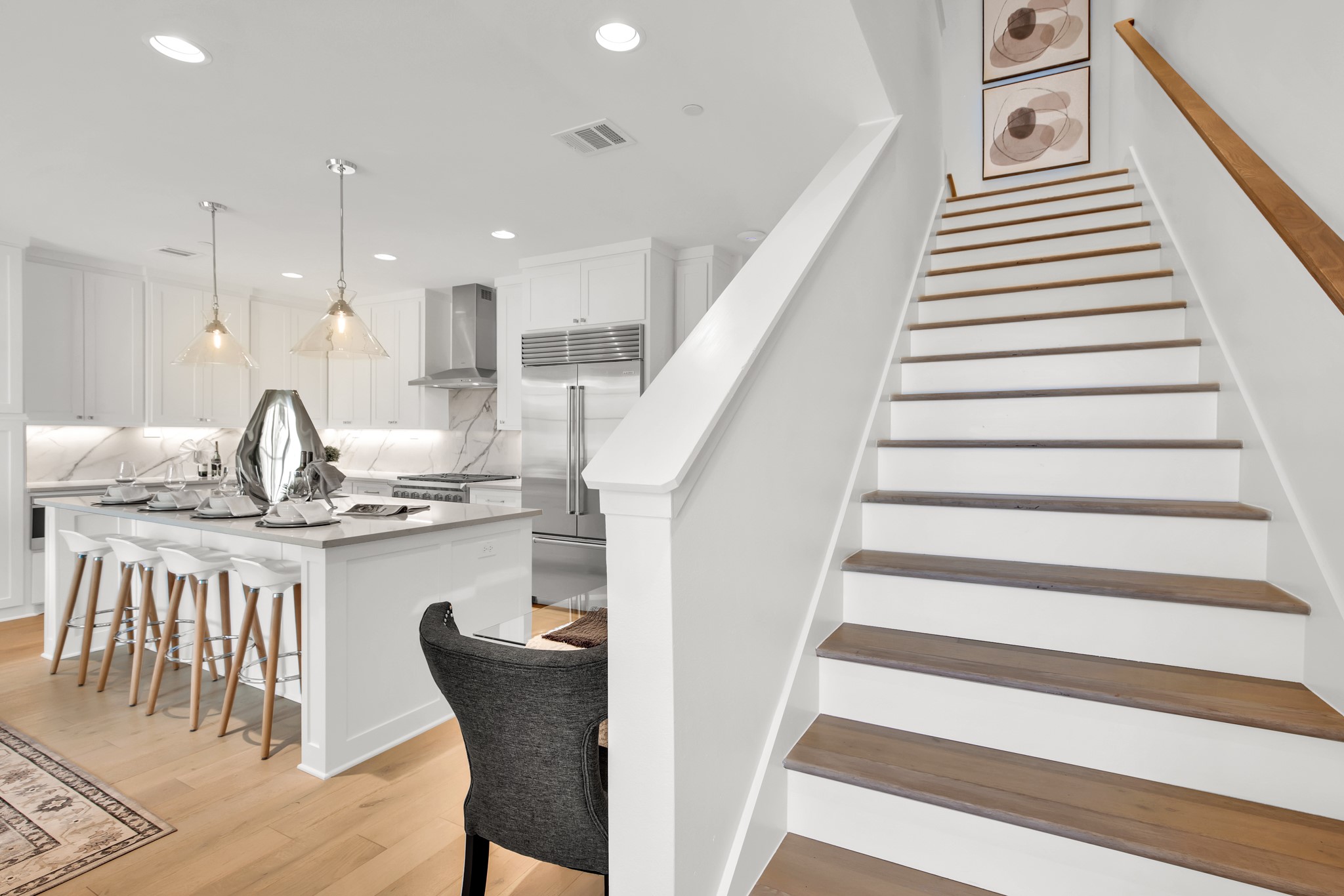 Staged white kitchen with a large island beside a staircase with dark wood treads.
