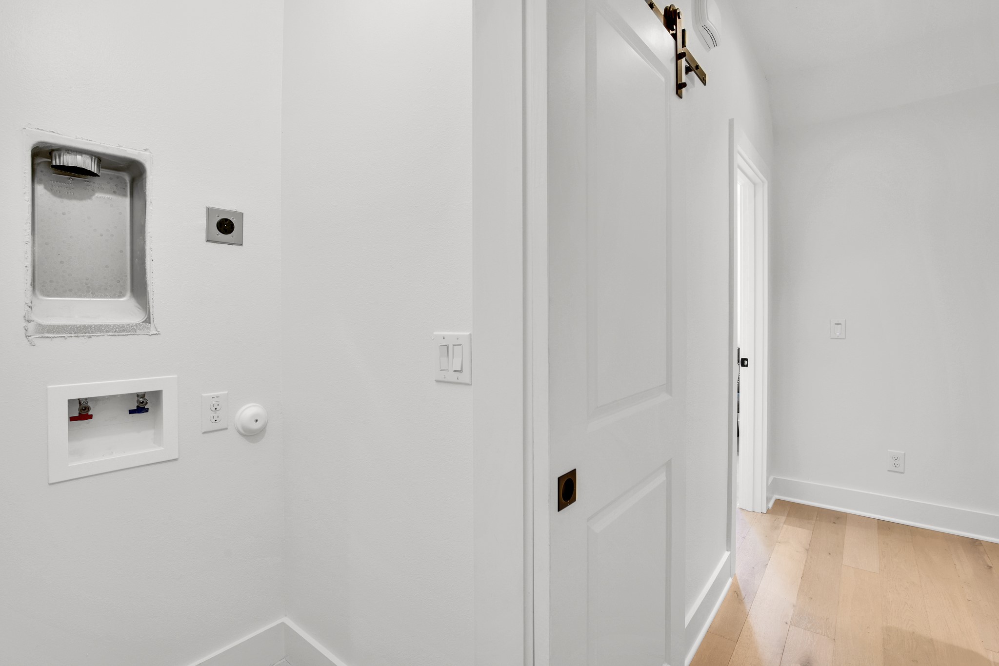 Laundry area with recessed washer hookups and a white paneled door beside light wood flooring.