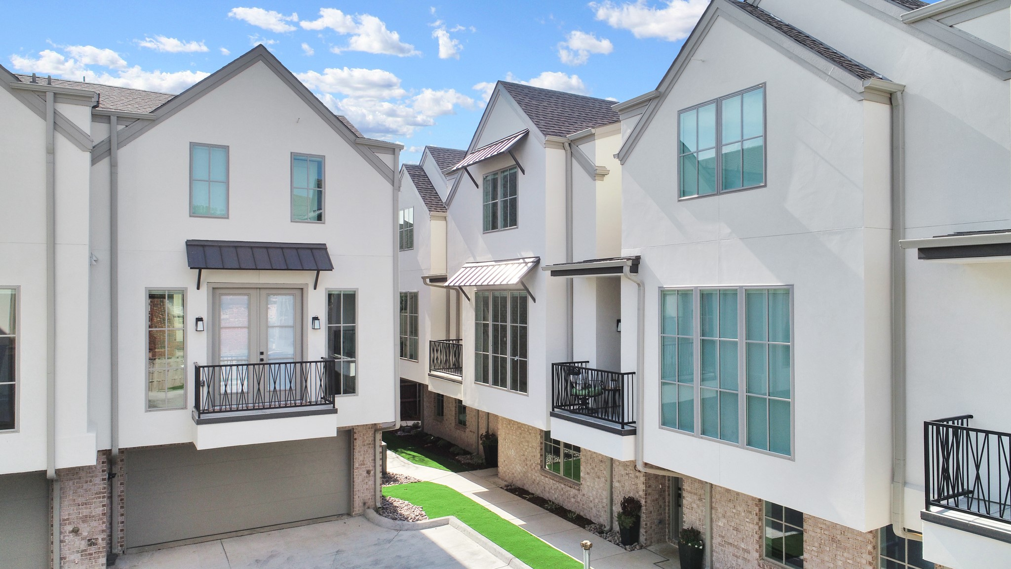 Modern white townhomes with balconies and large windows around a shared walkway.