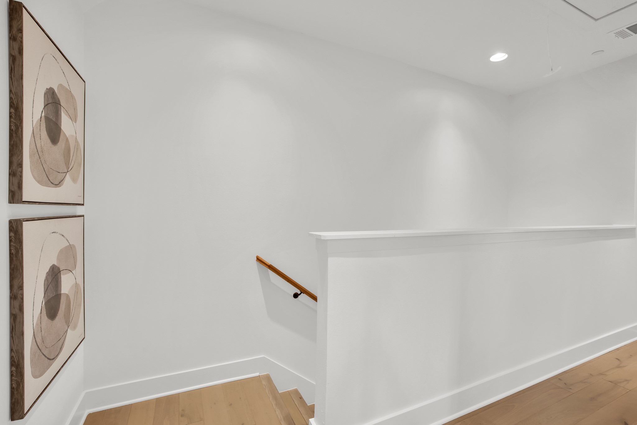 Bright stair landing with pale wood floors, a wooden handrail, and two framed abstract prints.