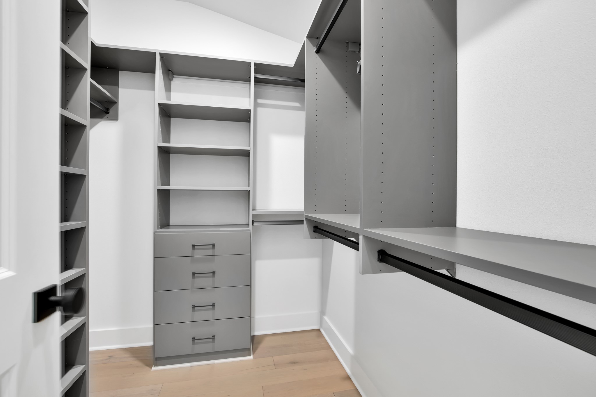 Walk-in closet with gray built-in shelves and drawers, hanging rails, and light wood flooring.