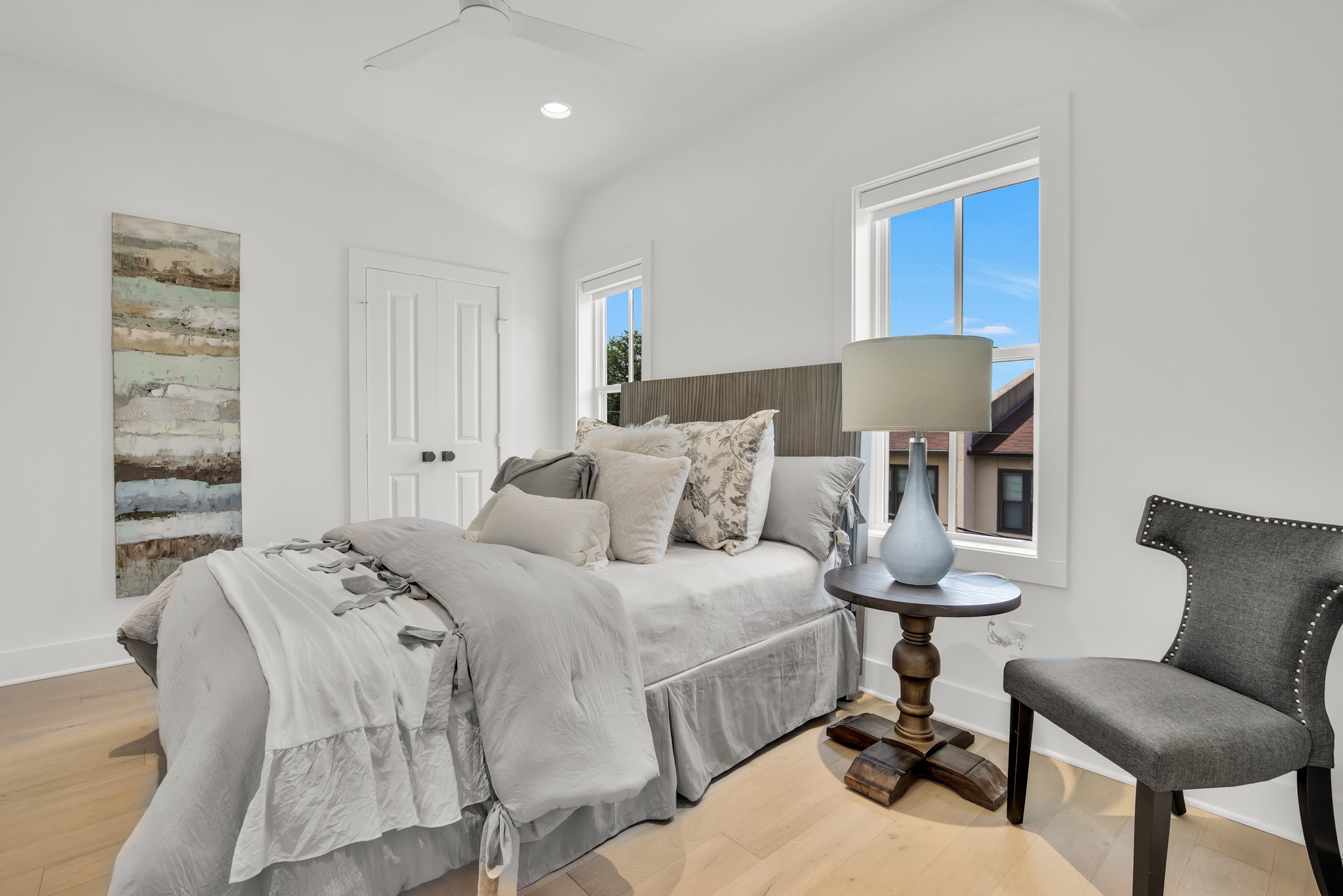 Furnished bedroom with a layered white bed, tall windows, and a dark upholstered chair.