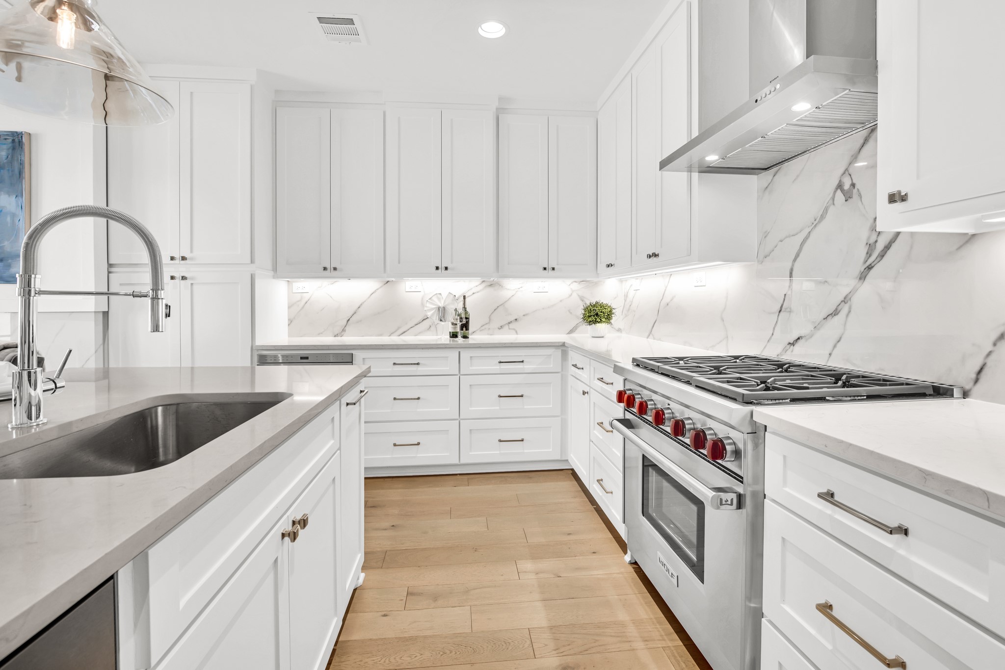 Kitchen with white cabinets, veined stone surfaces, a stainless steel range, and light wood flooring.