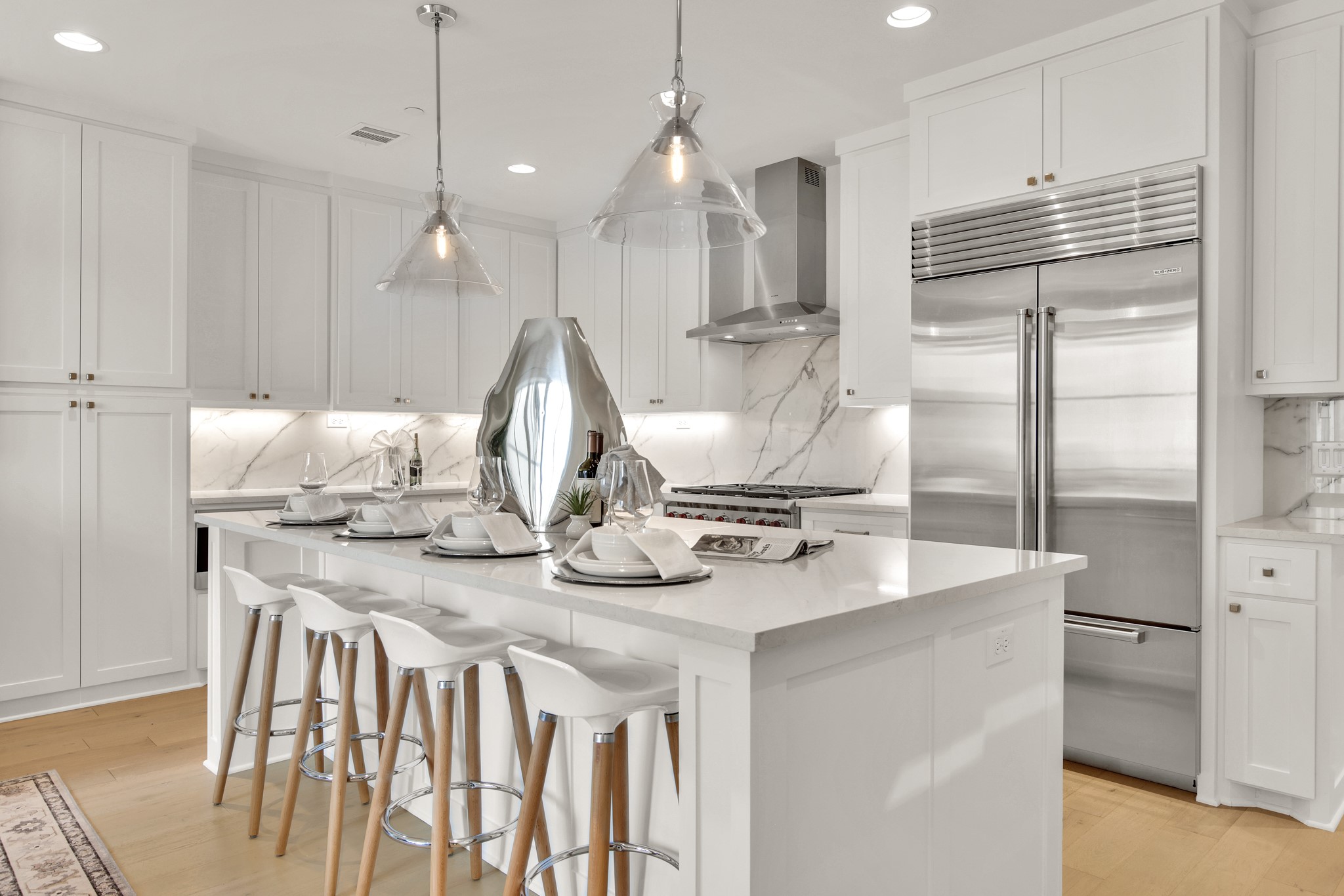 White kitchen with marble island, place settings, bar stools, and stainless-steel appliances.