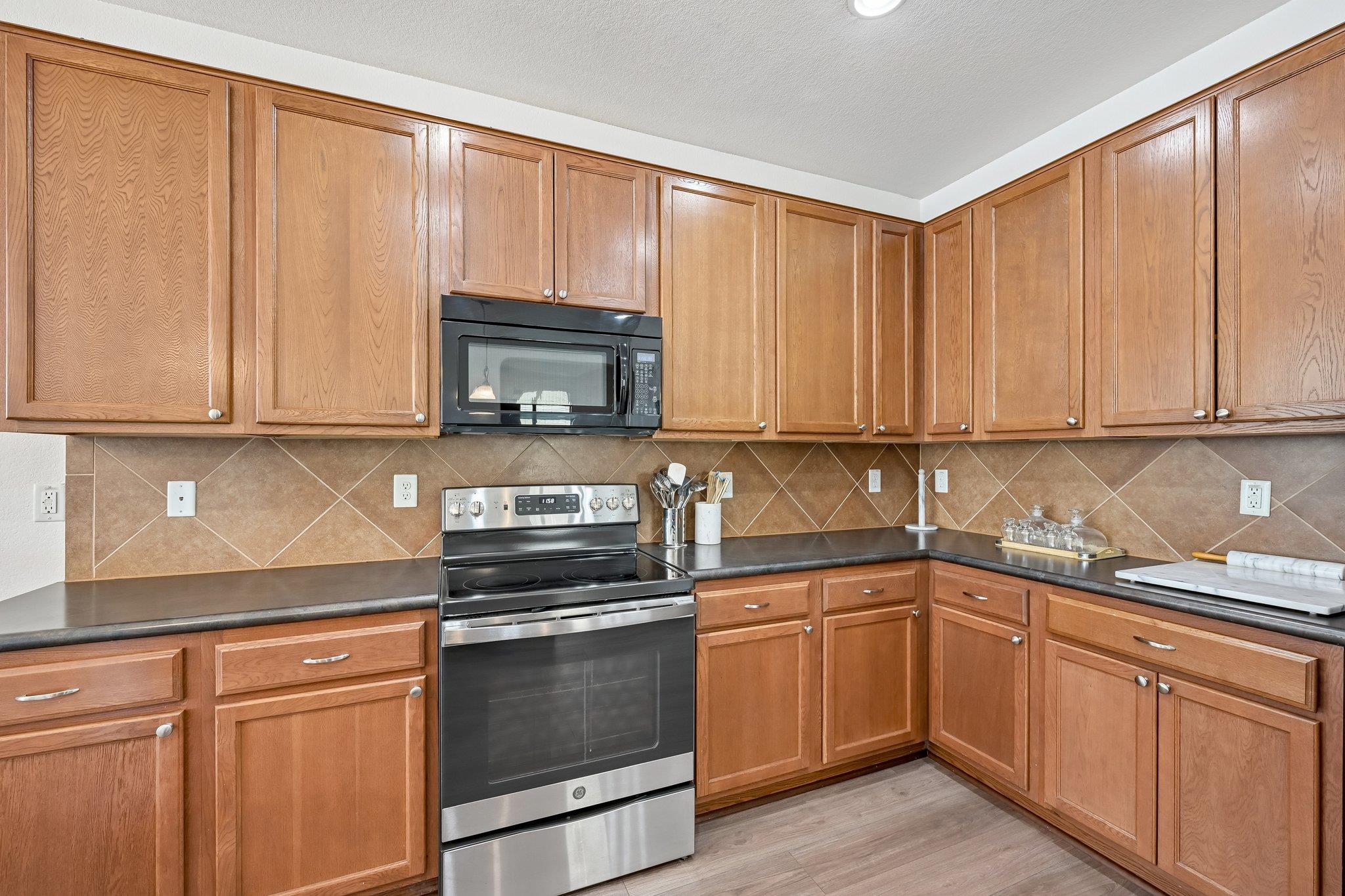Kitchen with warm wood cabinets, dark countertops, and a stainless steel range and microwave.