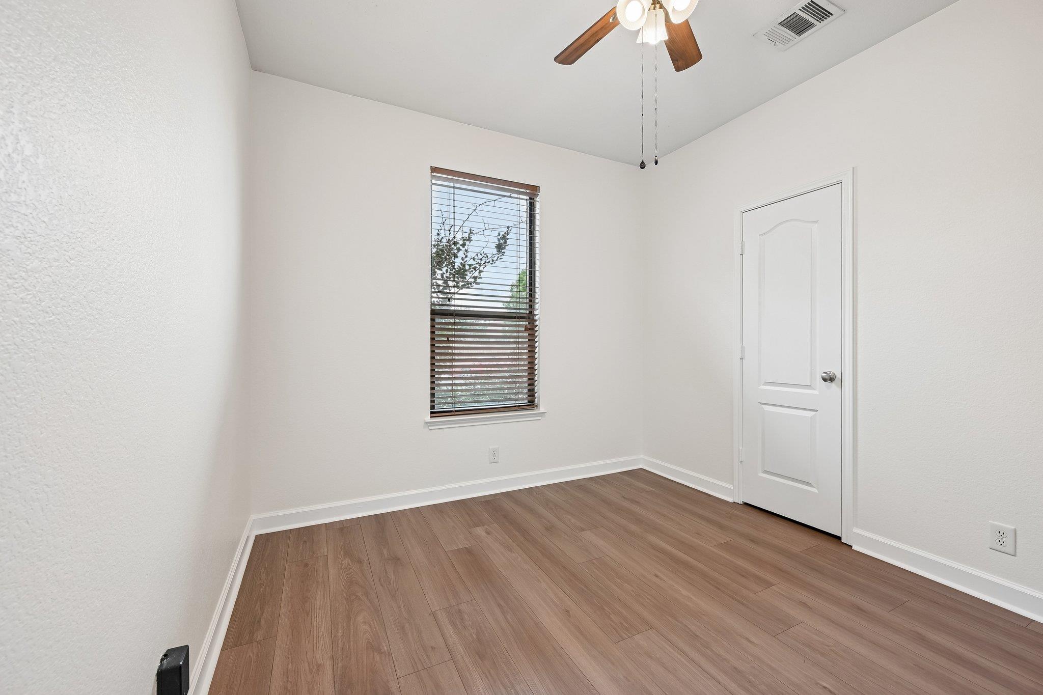 Empty room with wood-look floors, a window with blinds, and a ceiling fan.